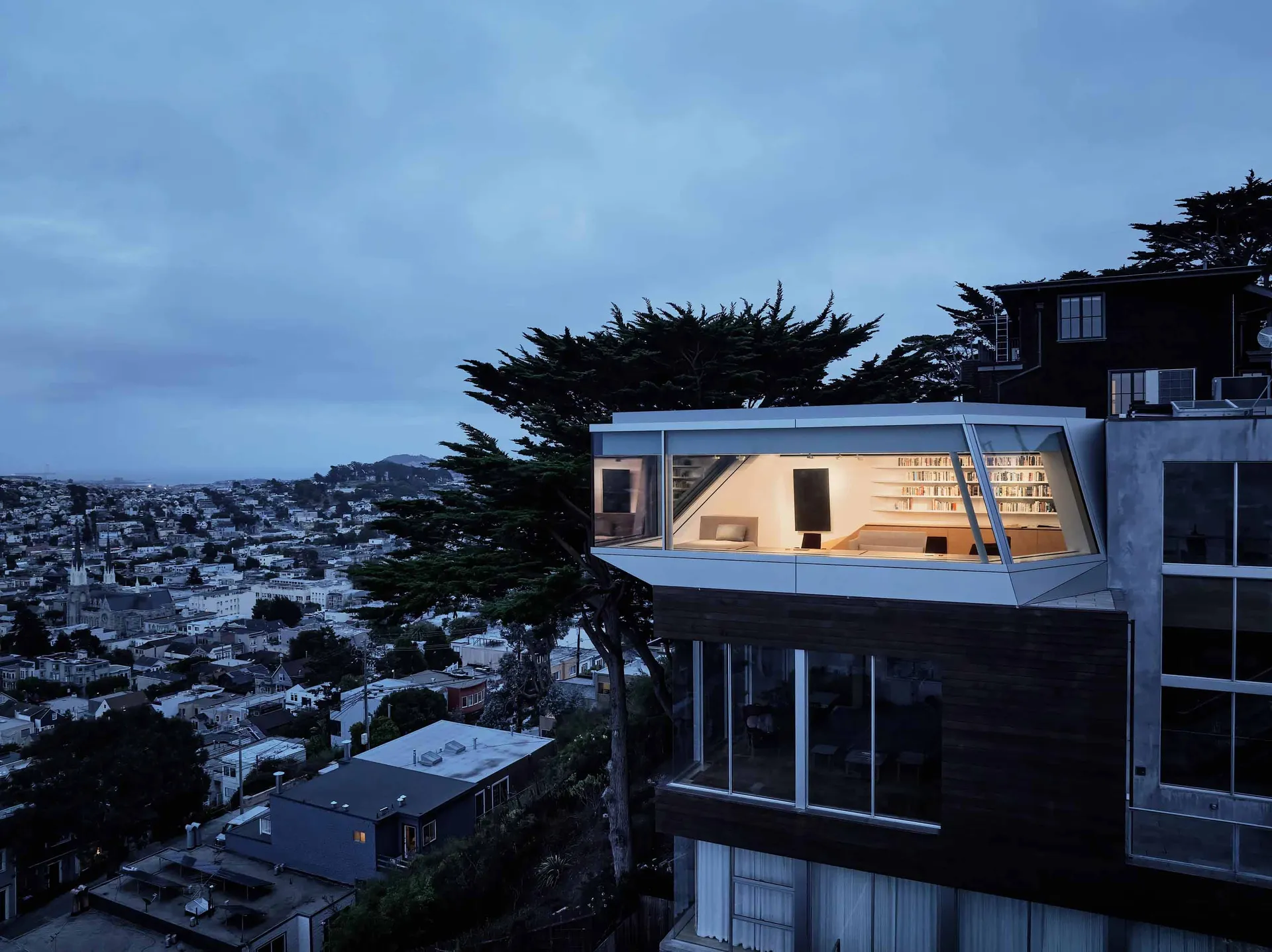 A modern house with a glass extension overlooking a cityscape at dusk.