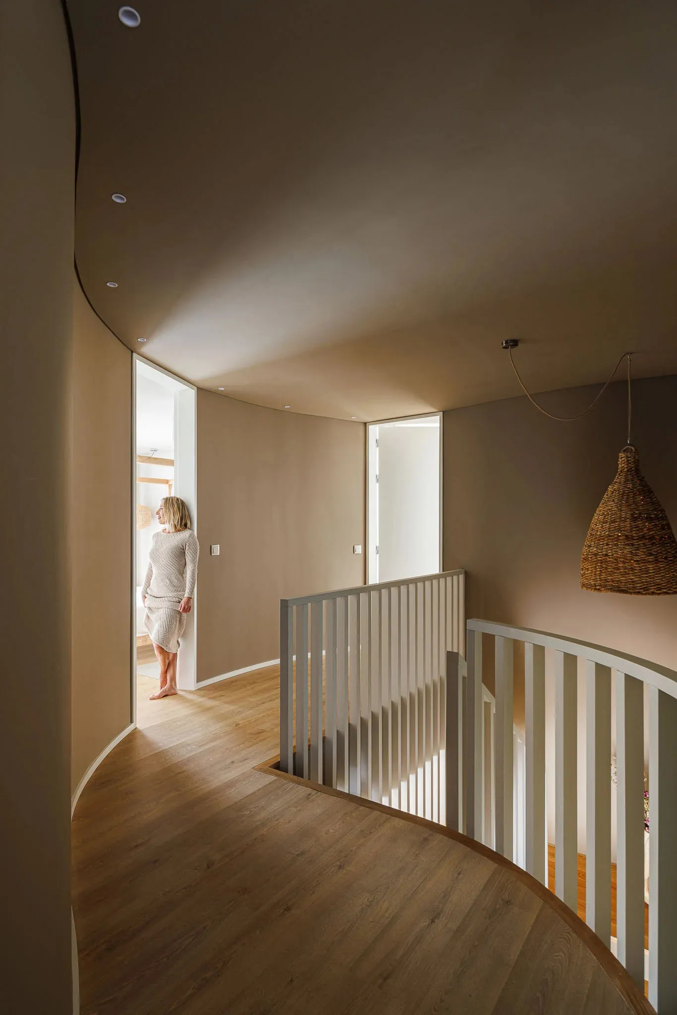 A minimalist residential interior with wooden flooring, rich tan painted walls, and white railings.