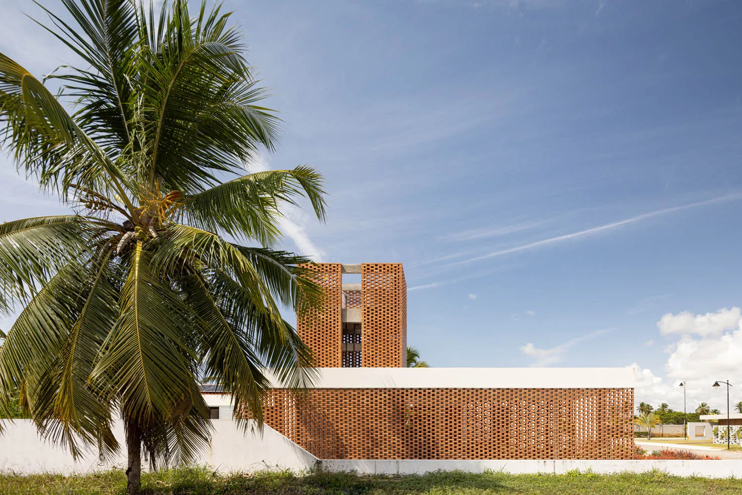 A modern brick building with a palm tree in the foreground against a blue sky.