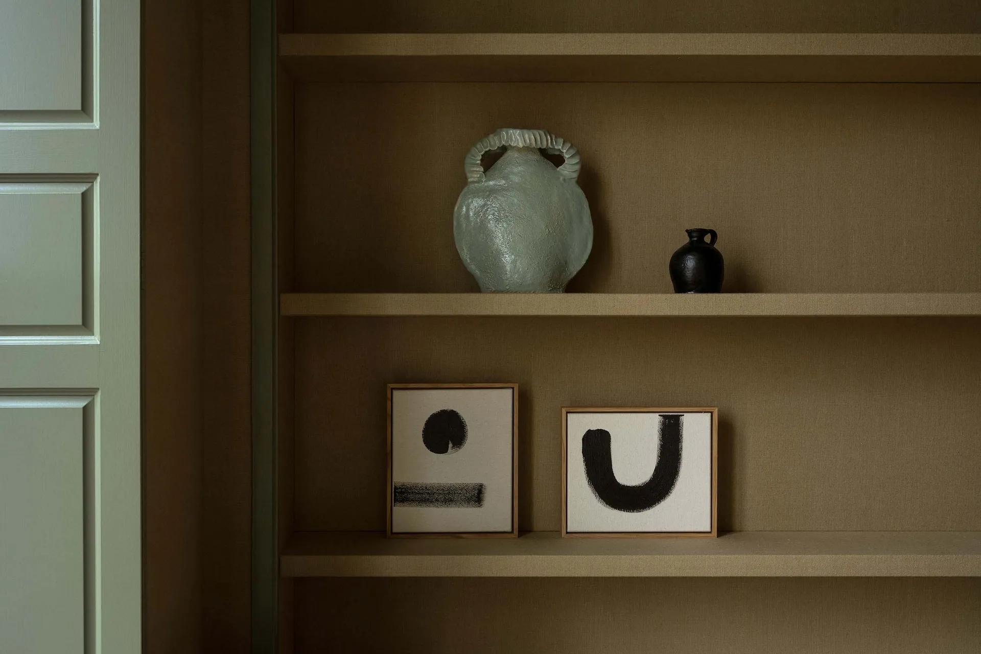 Modern interior design featuring a ceramic vase and abstract paintings on shelves.