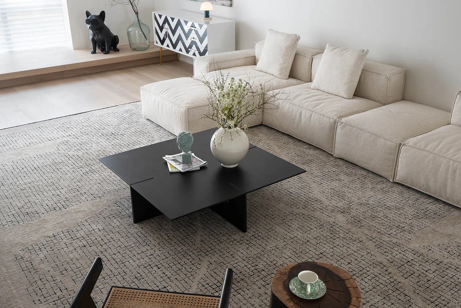 Minimalist design living room featuring beige sectional sofa, black square coffee table, and textured rug
