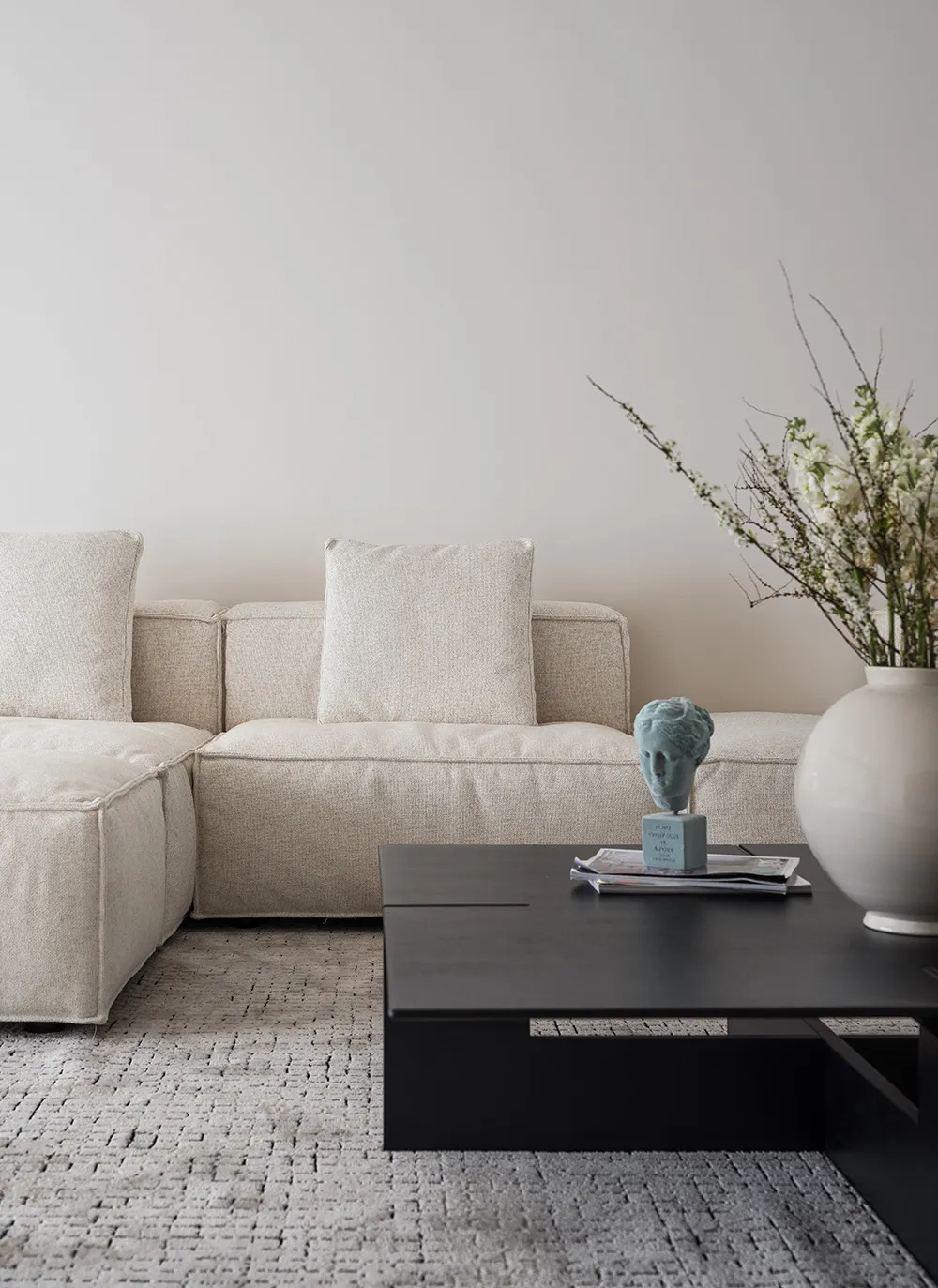 A minimalist living room featuring a fabric sofa with a coffee table and decorative vase.