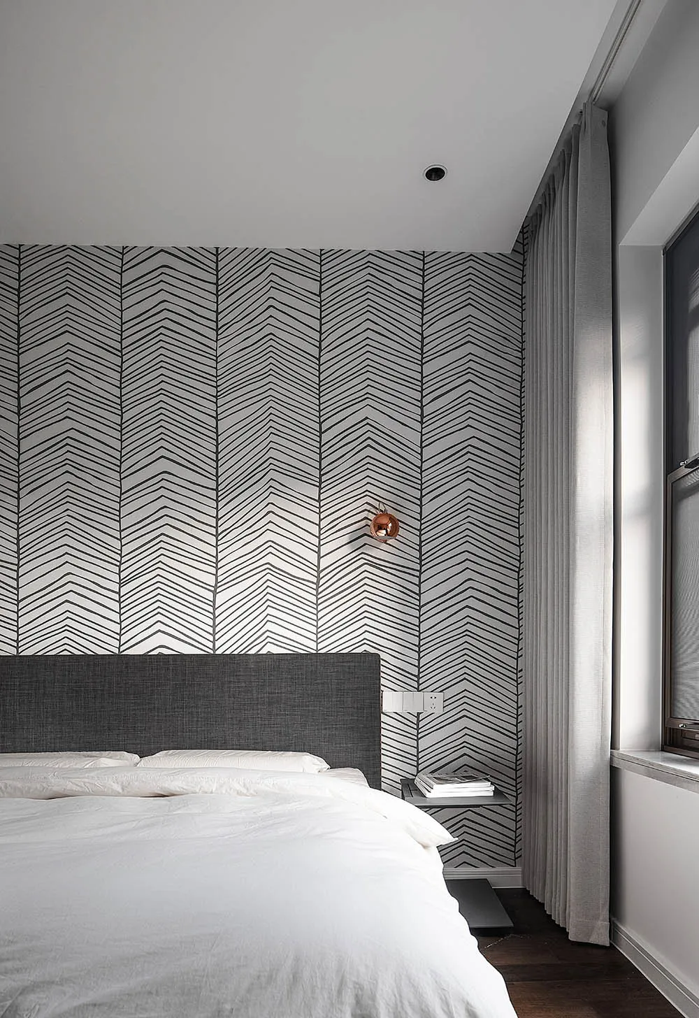 Modern, minimalist bedroom with a grey fabric headboard, white bedding, and geometric wallpaper.
