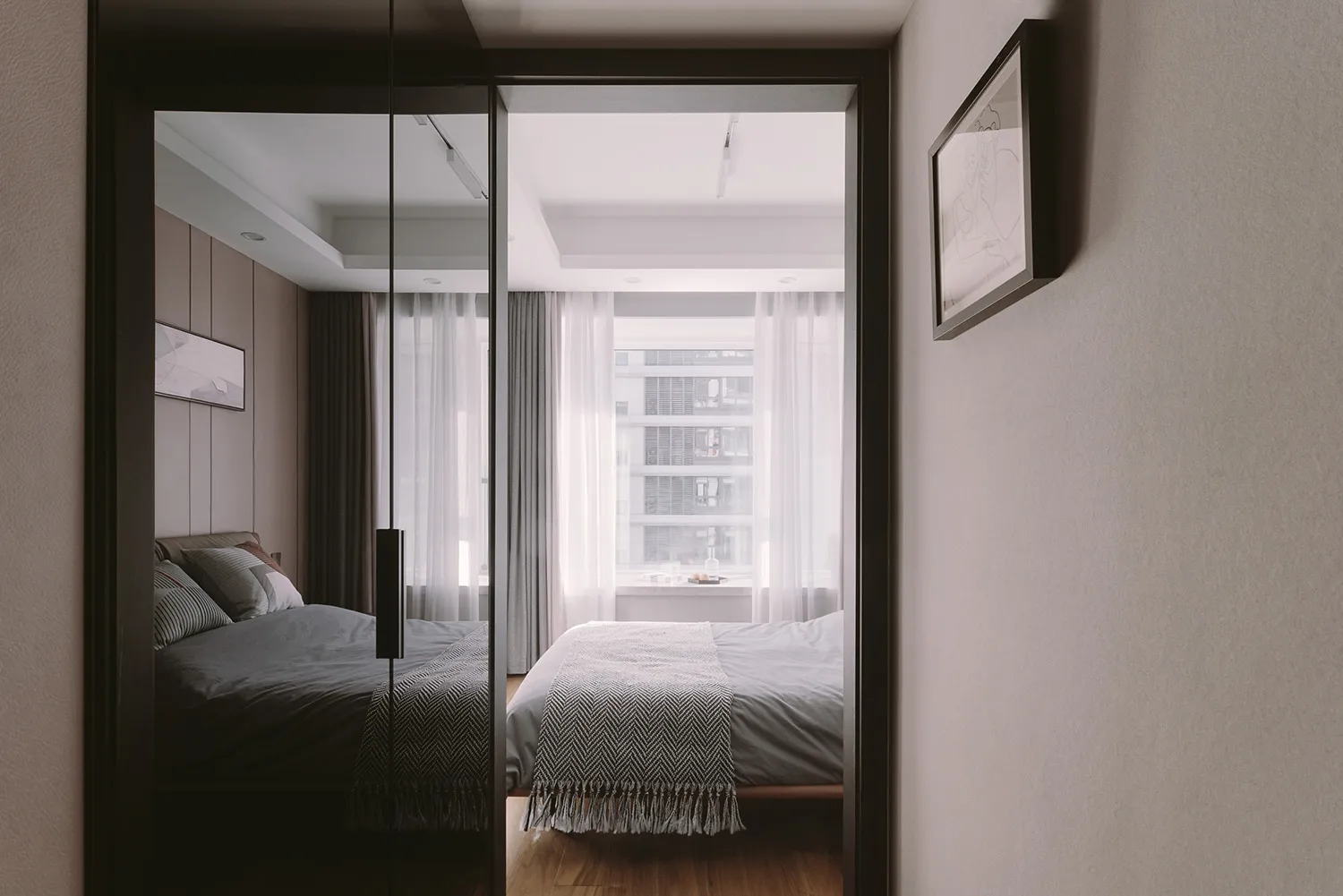 A minimalist bedroom featuring a bed with white curtains and a grey bedspread, set against a grey wall and hardwood floor.