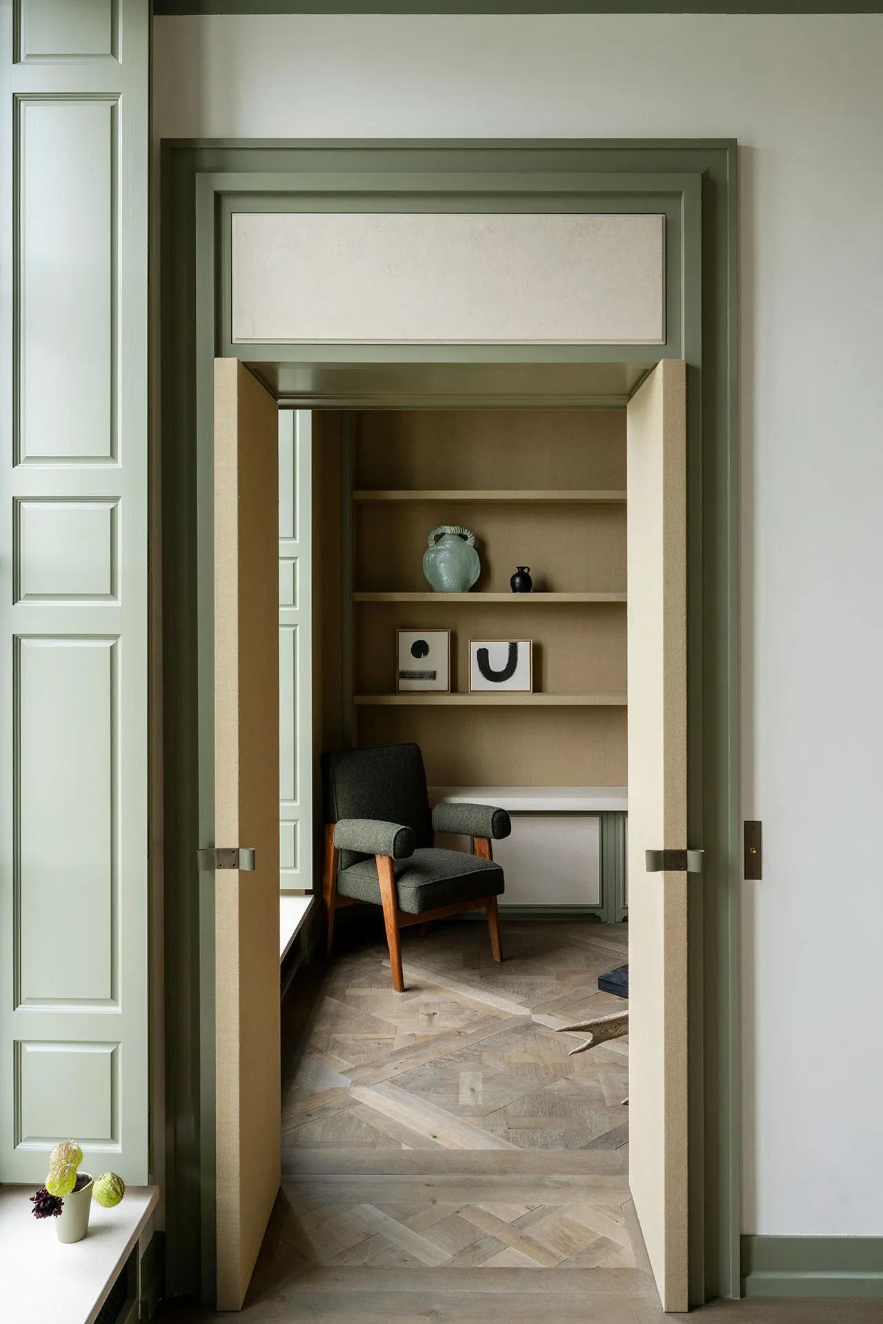 A minimalist office space with a wooden parquet floor, shelving, and a comfortable chair.