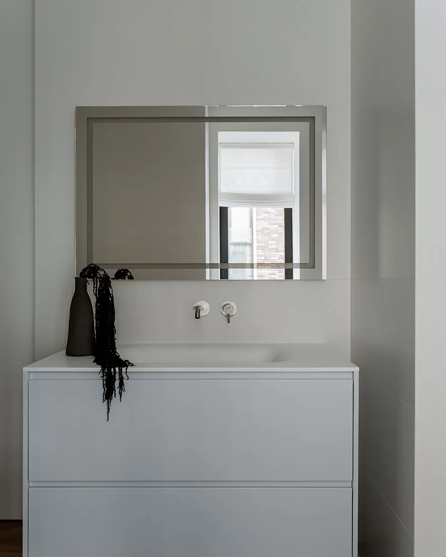 Minimalist bathroom with a white ceramic sink, glass wall, and metal fixtures.