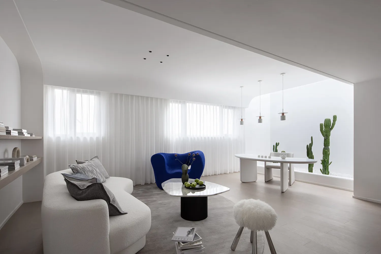 A modern minimalist living room featuring a white couch, blue accent chair, and glass coffee table with a vase and green appl