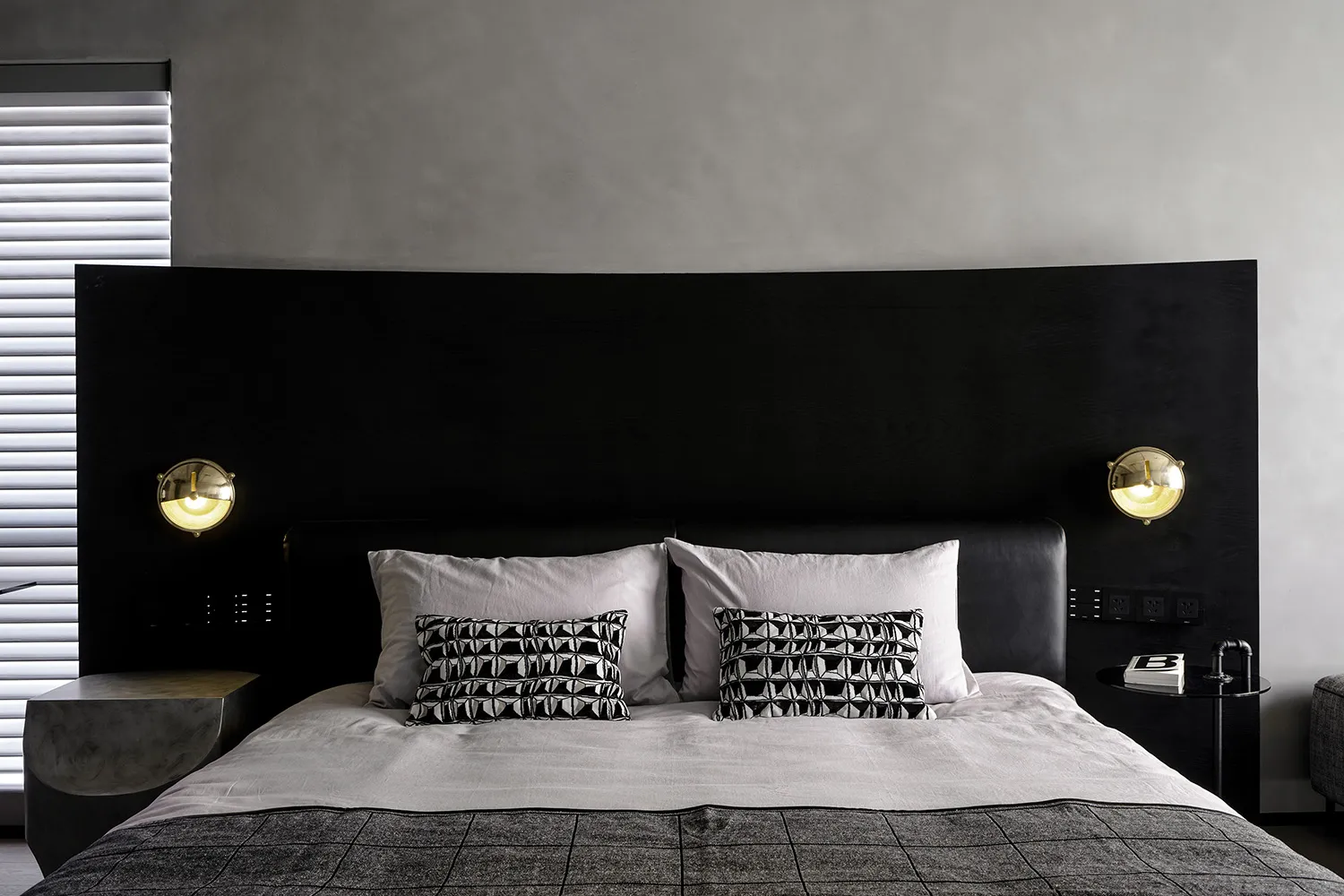 A modern bedroom featuring a black wooden headboard and a bed with white linens and patterned pillows.