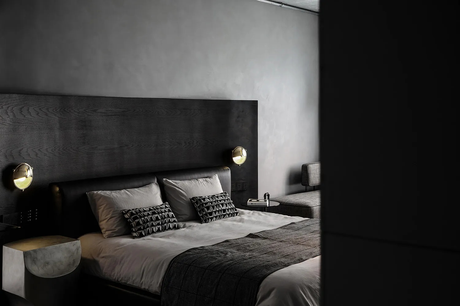 A minimalist bedroom with a dark wood headboard and light bedding, featuring modern sconce lighting and a sleek, low-profile