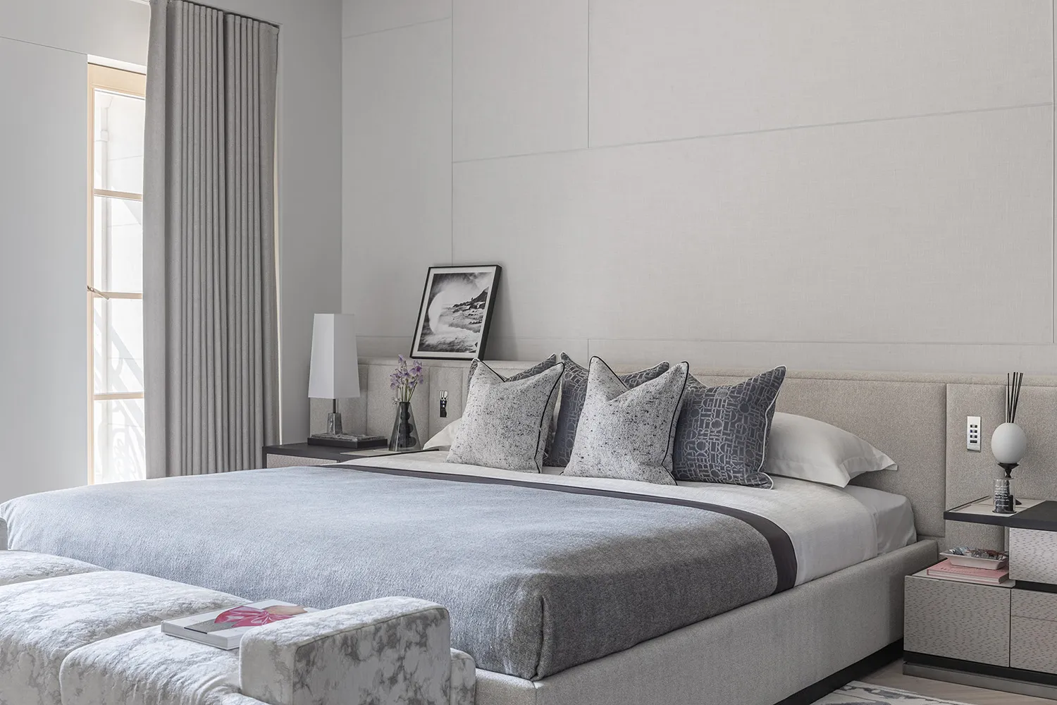Modern minimalistic bedroom featuring upholstered furniture, neutral color palette, and abstract artwork.