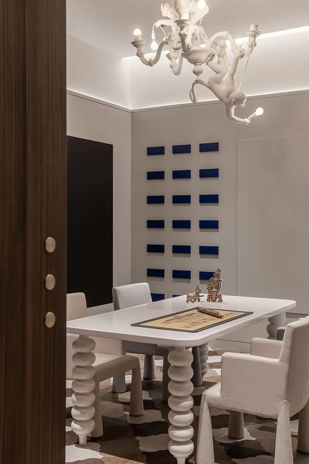 A modern dining room features a white-painted table and chairs with a decorative chandelier hanging above it.