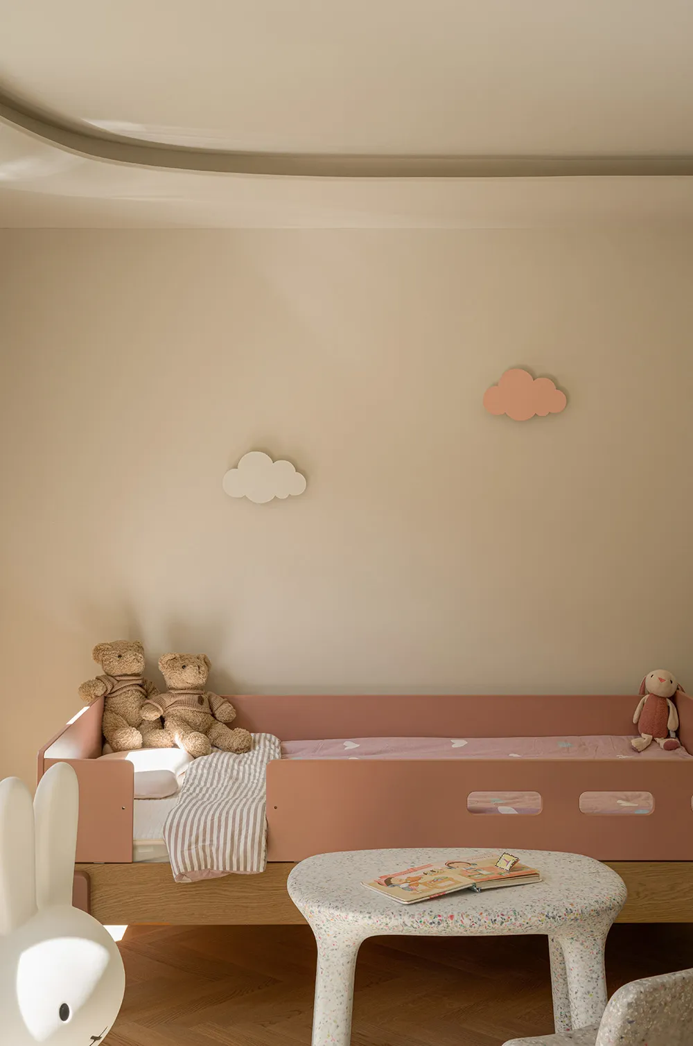 A minimalist child's bedroom featuring a wooden bunk bed with fabric bedding and stuffed animals.