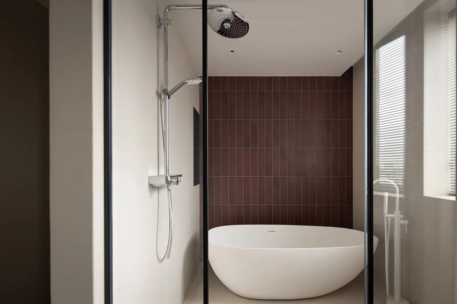 A modern bathroom featuring a white freestanding bathtub, a dark brown tiled wall, and a walk-in shower with a glass enclosur