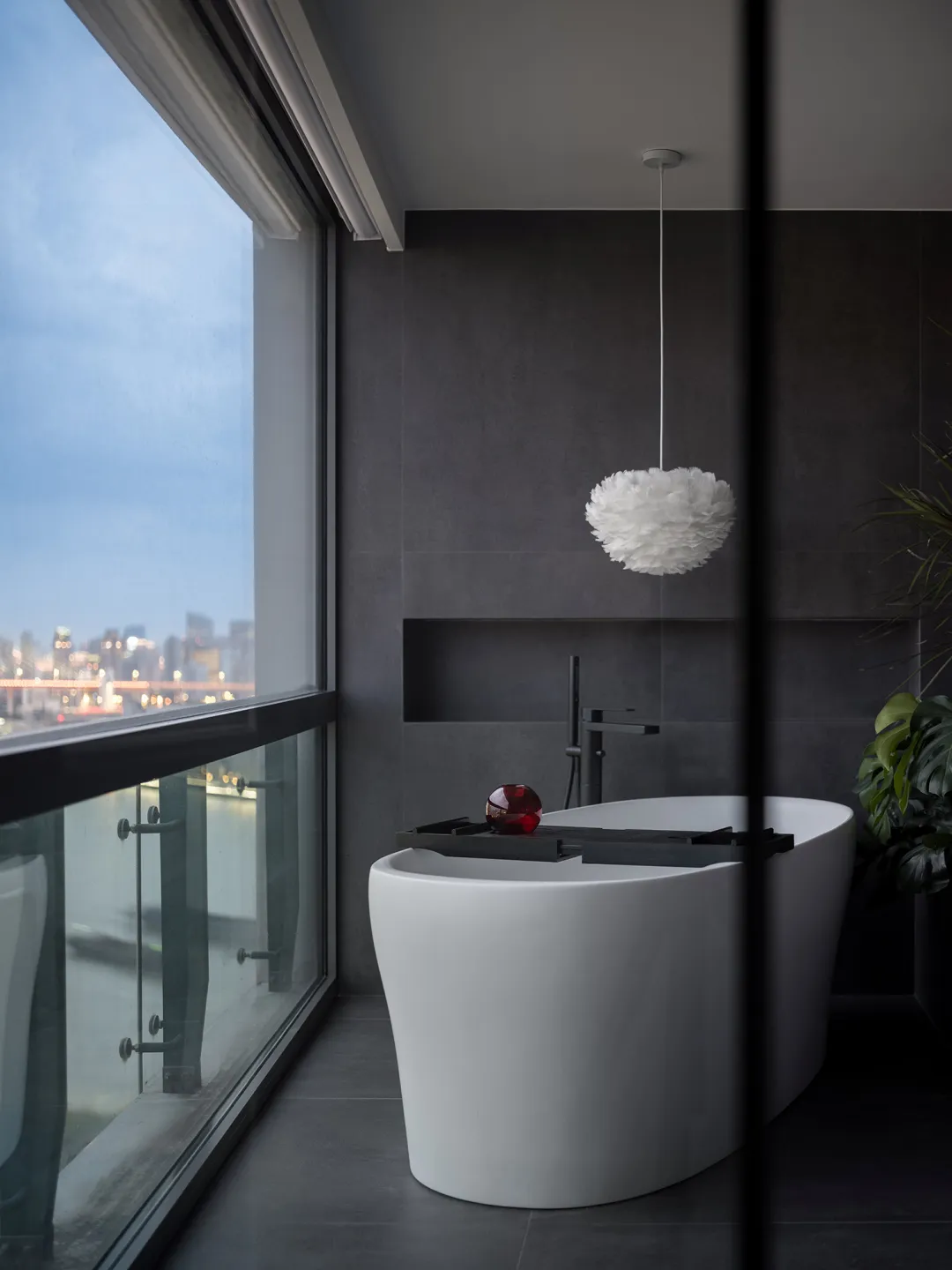 Modern bathroom featuring a freestanding bathtub made of white concrete with a red object on a tray and a white pendant lamp