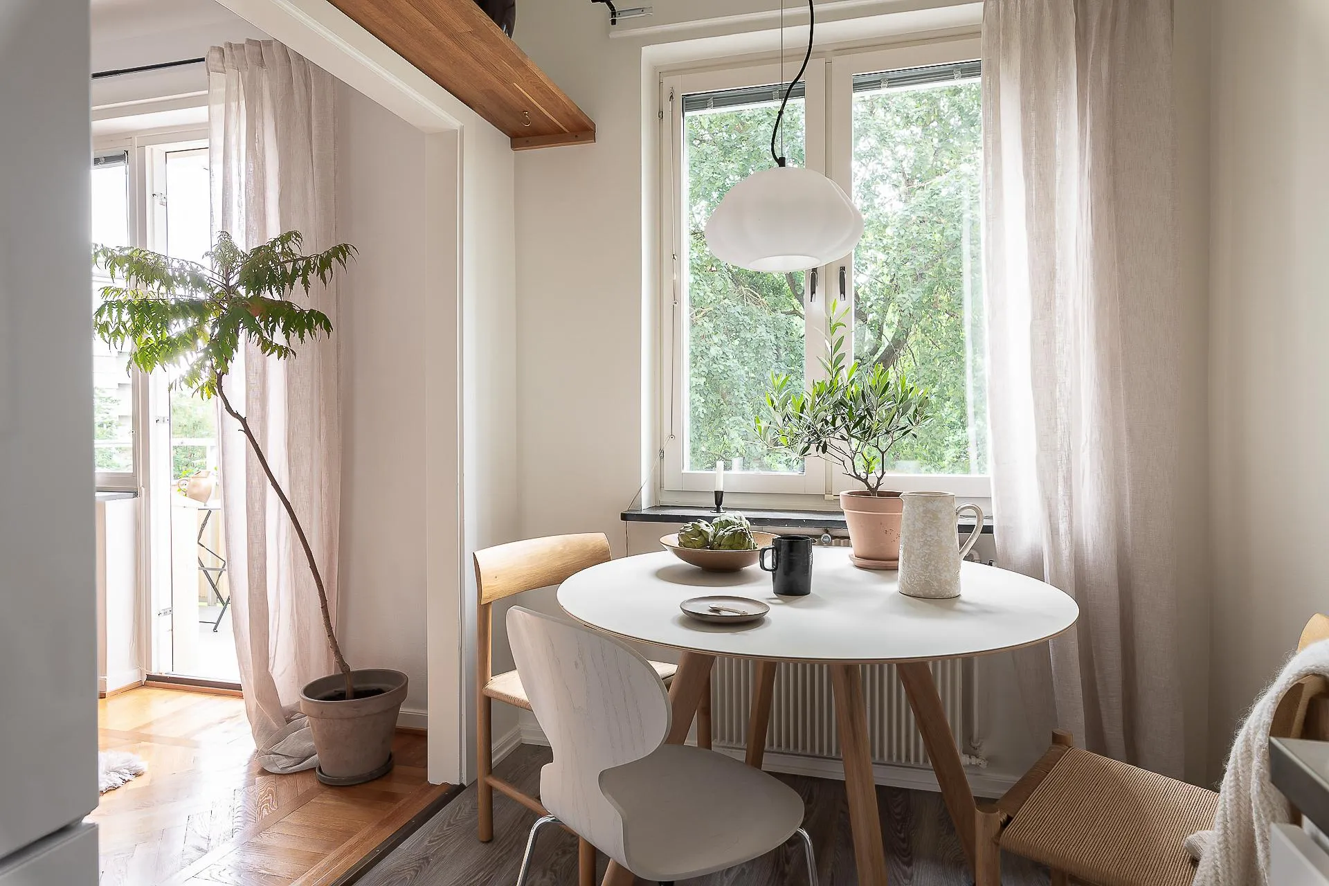 A minimalist interior with a wooden dining table, white chairs, and decorative plants by the window.