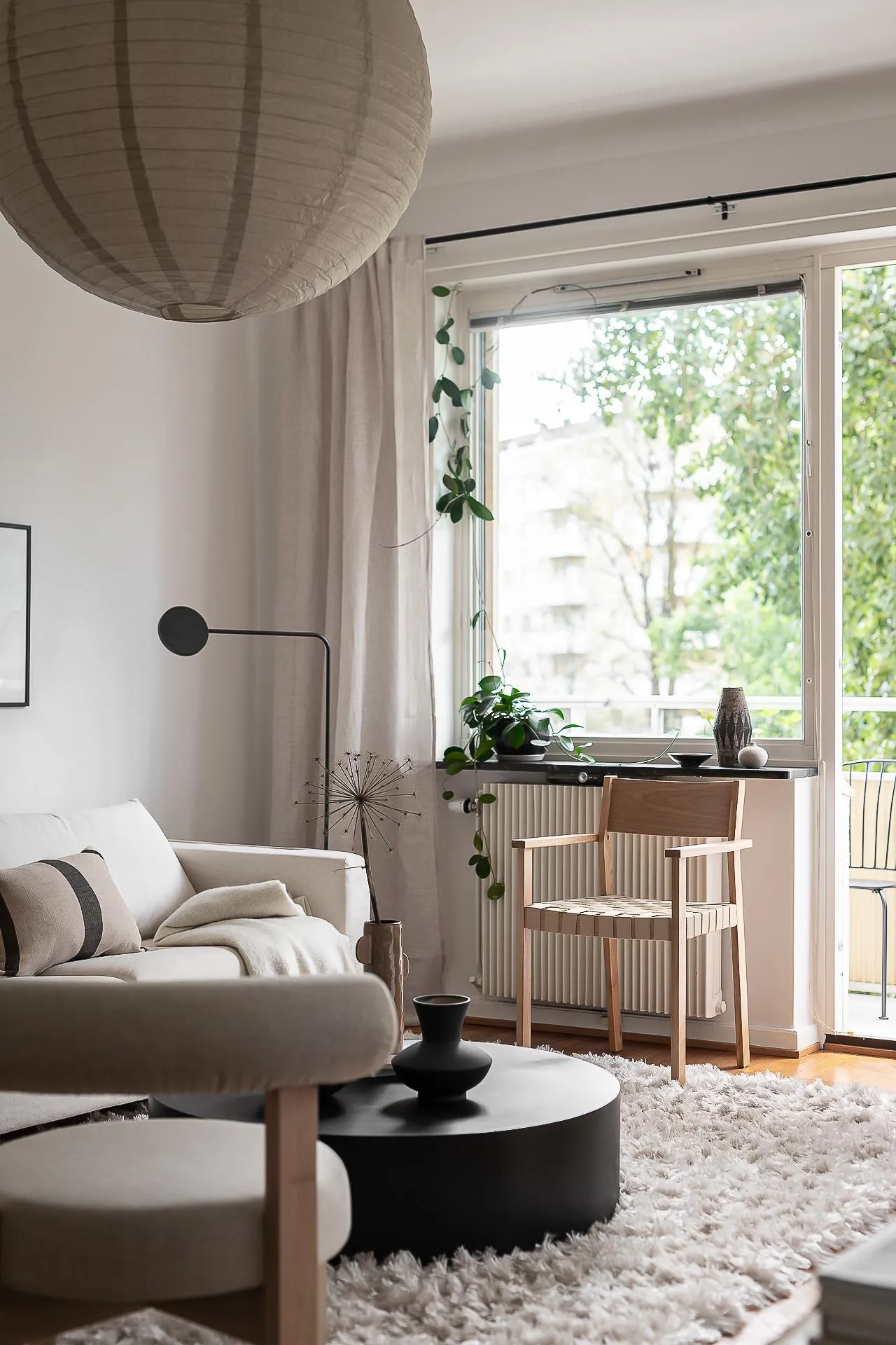 A minimalist living room featuring a couch, coffee table, and window with greenery outside.
