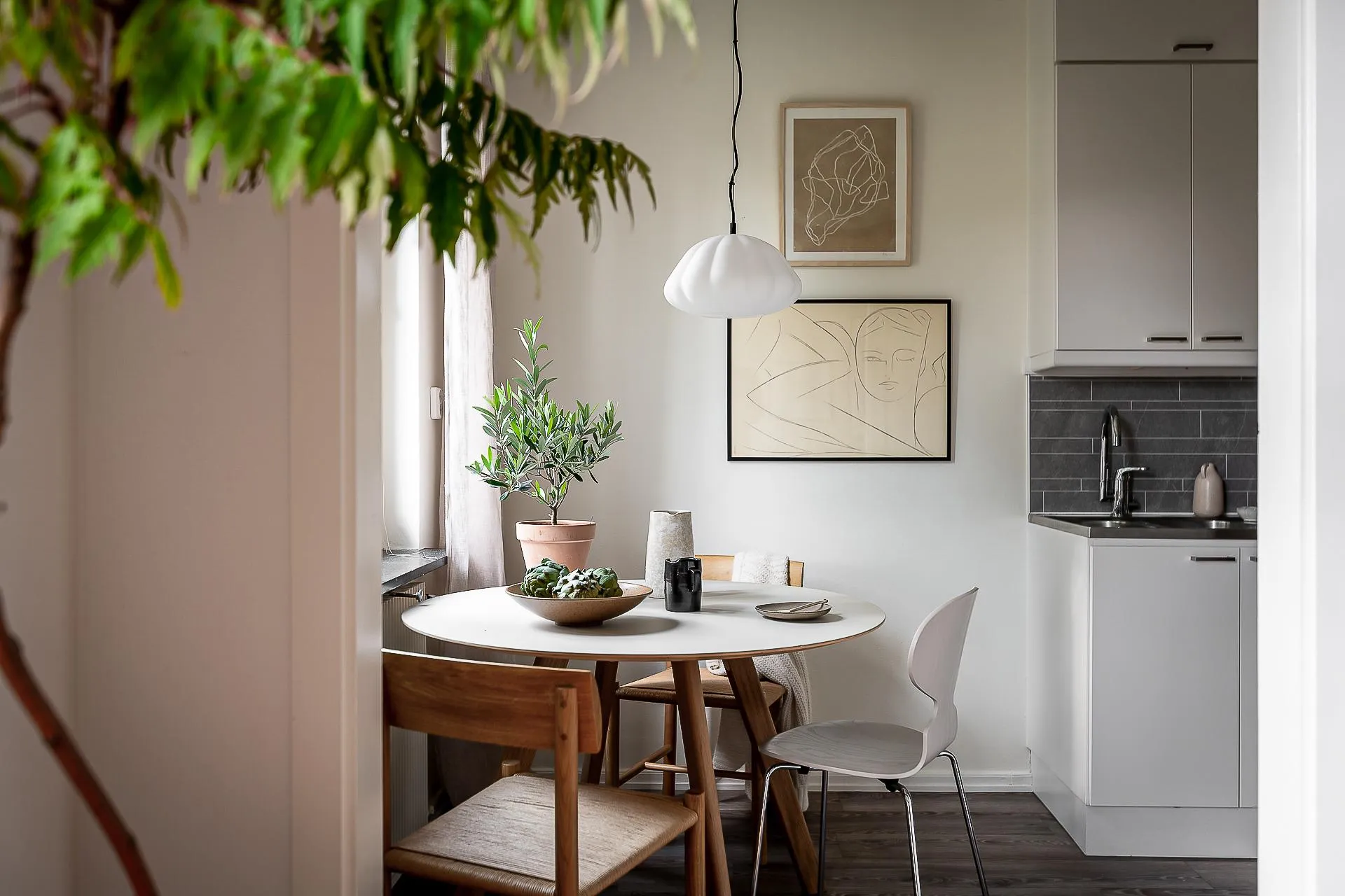 A minimalist kitchen with white furniture, a round table, and a white pendant light hanging above it.