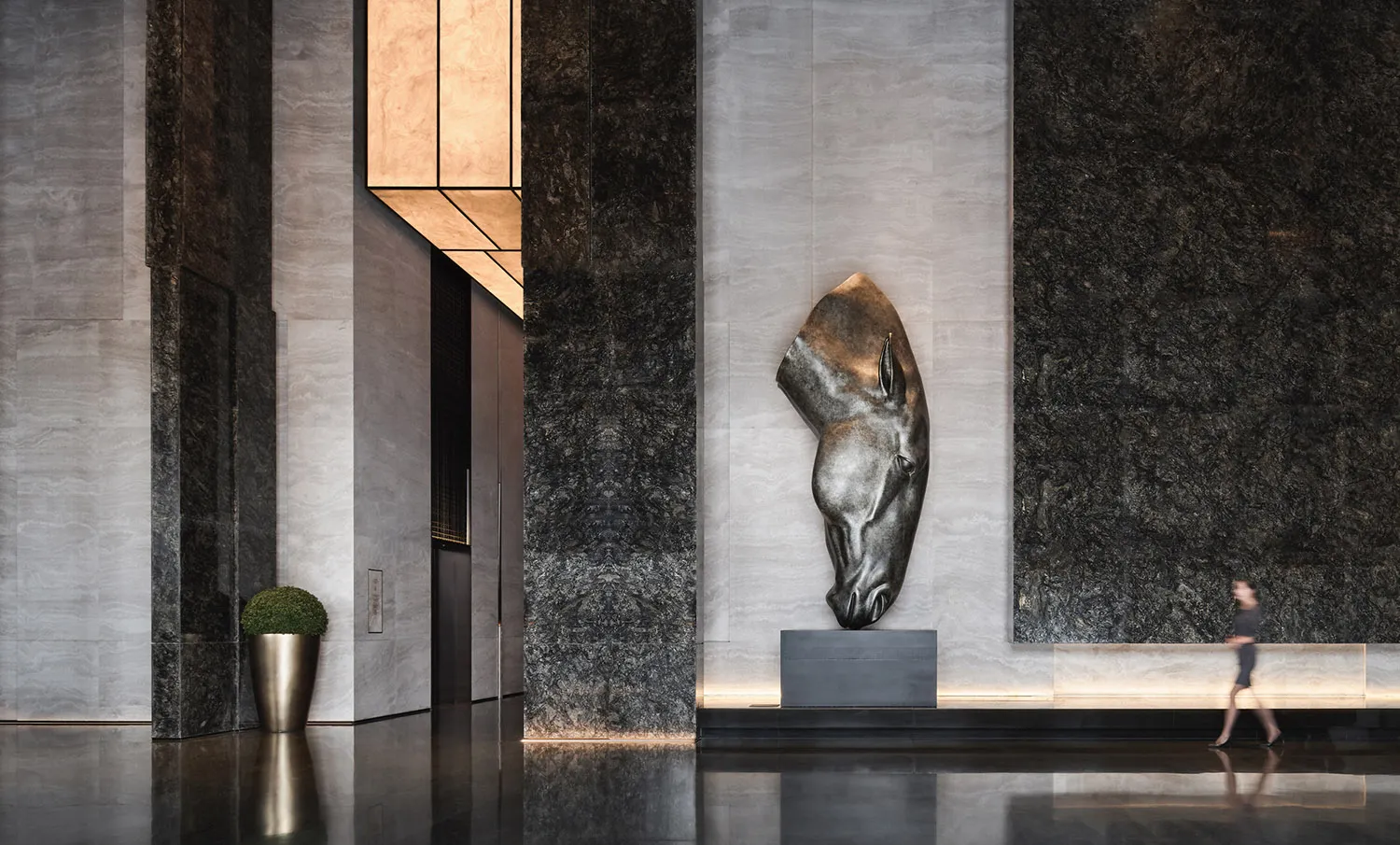 A modern lobby interior featuring a metallic sculpture of a horse's head mounted on the wall, set against a backdrop of polis
