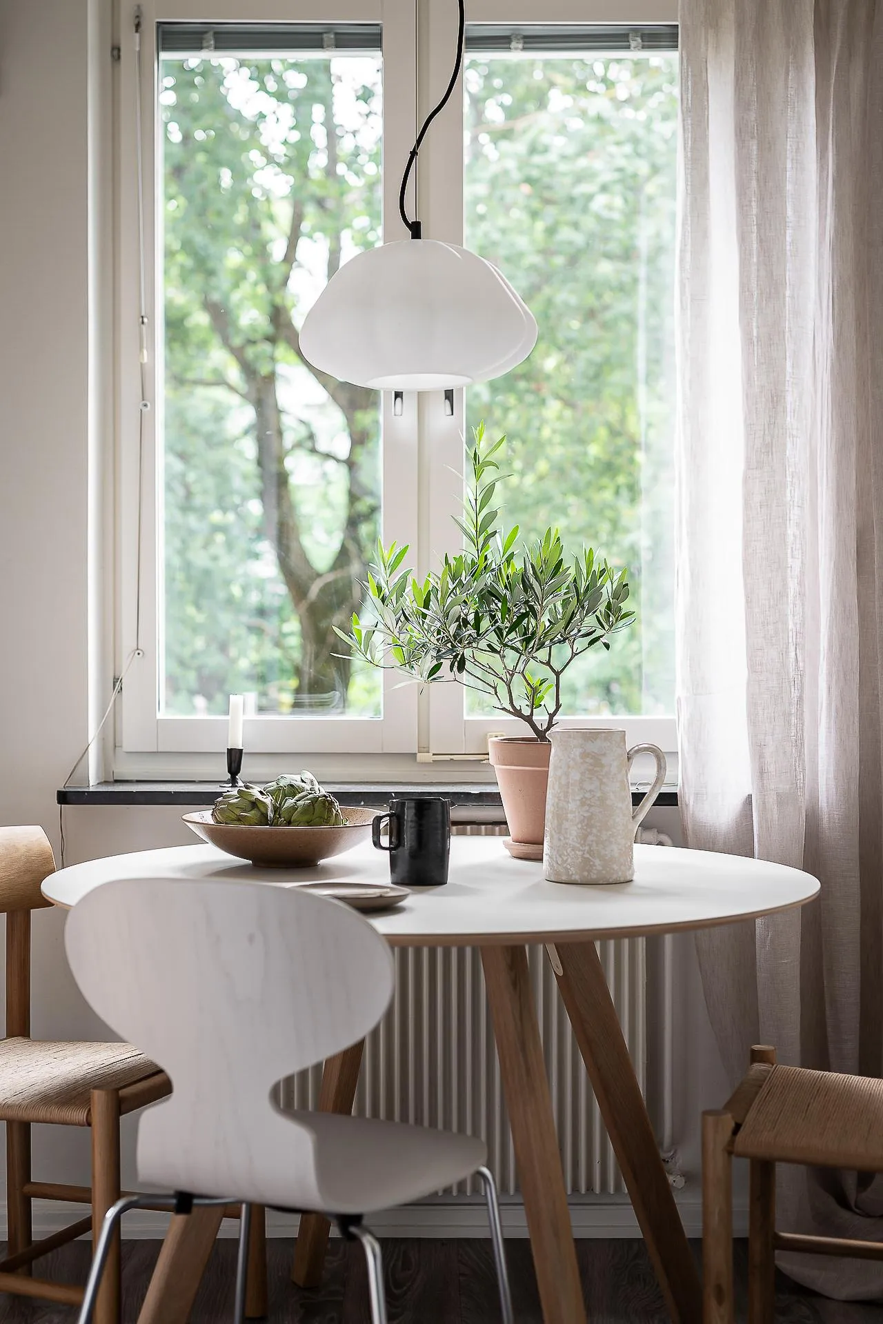 A modern minimalist kitchen with white cupboards, wooden furniture, and a wooden floor, featuring a round table with a vase a