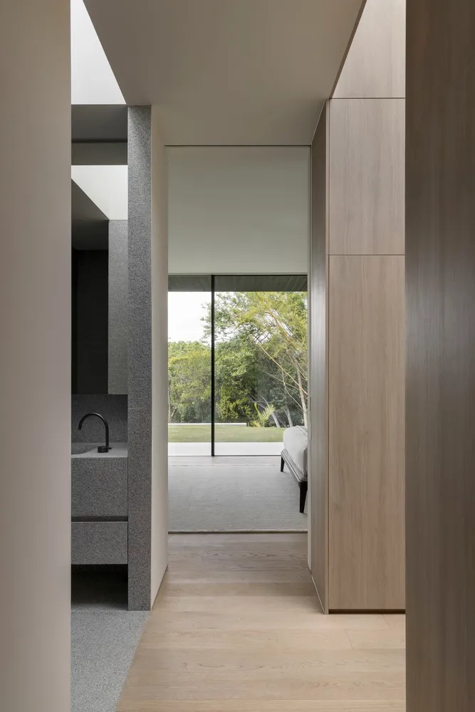 Modern minimalist living room with large wooden panels, minimalist furniture, and a glass wall overlooking greenery.