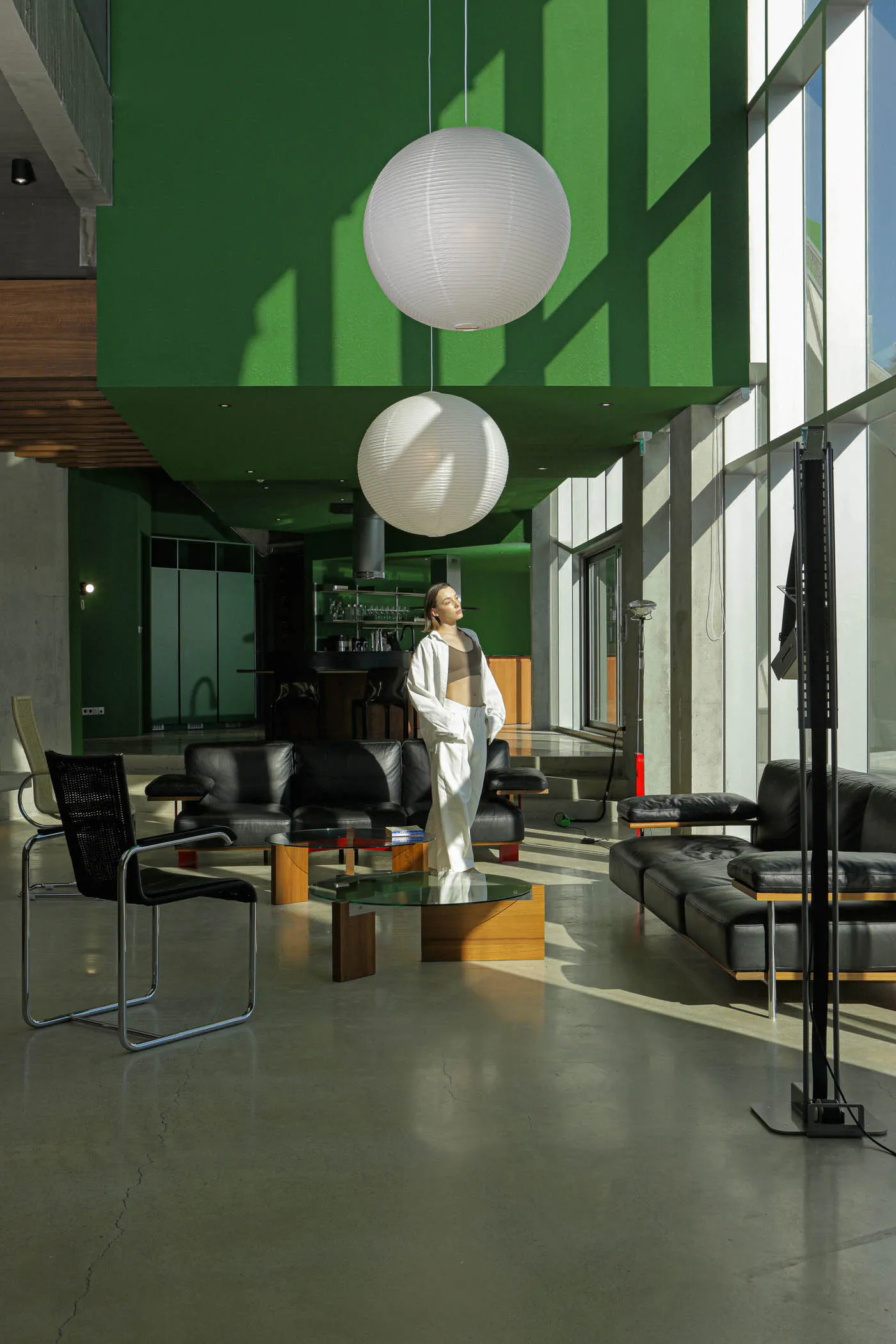 A modern minimalist living room with concrete walls, glass and metal furniture, and black leather sofas.