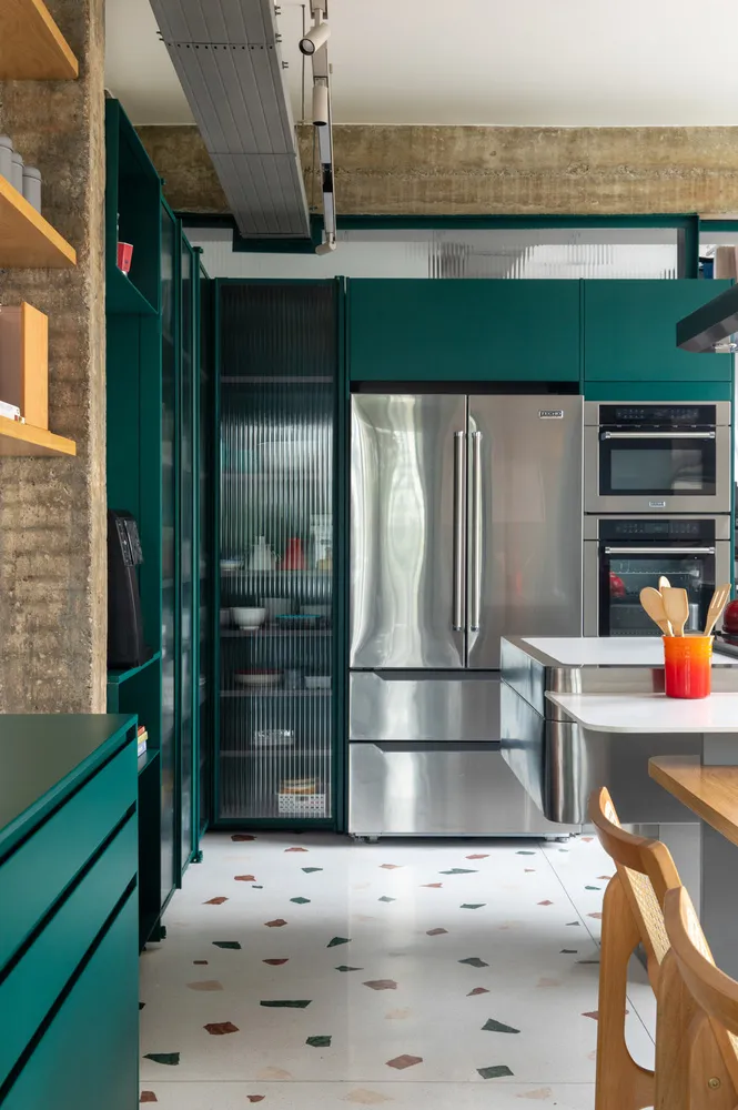 A modern industrial kitchen featuring stainless steel appliances, dark green cabinetry, and concrete flooring.