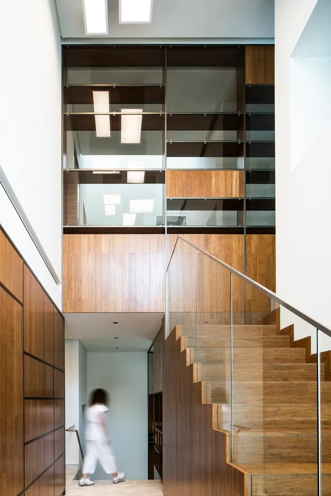 A modern staircase with wooden steps and a glass railing against a white wall, featuring a minimalist design.