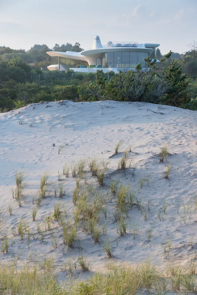 A modern house surrounded by dunes with glass walls and a white, futuristic design.