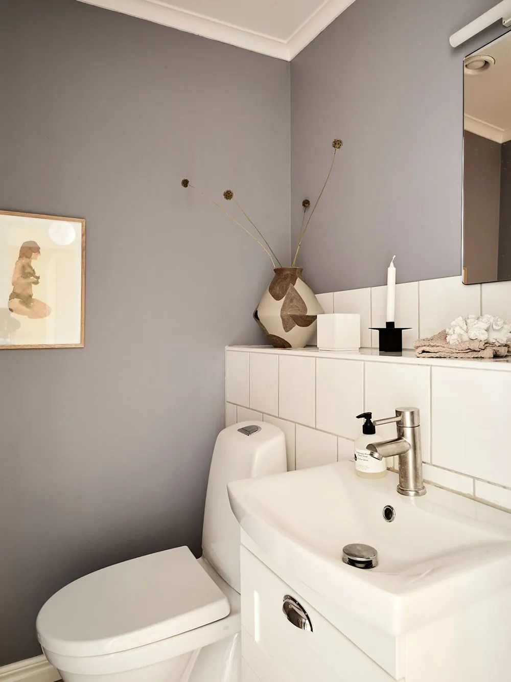 A minimalist grey bathroom interior with white ceramic tiles, a white toilet, and a white sink with a vase on the countertop.