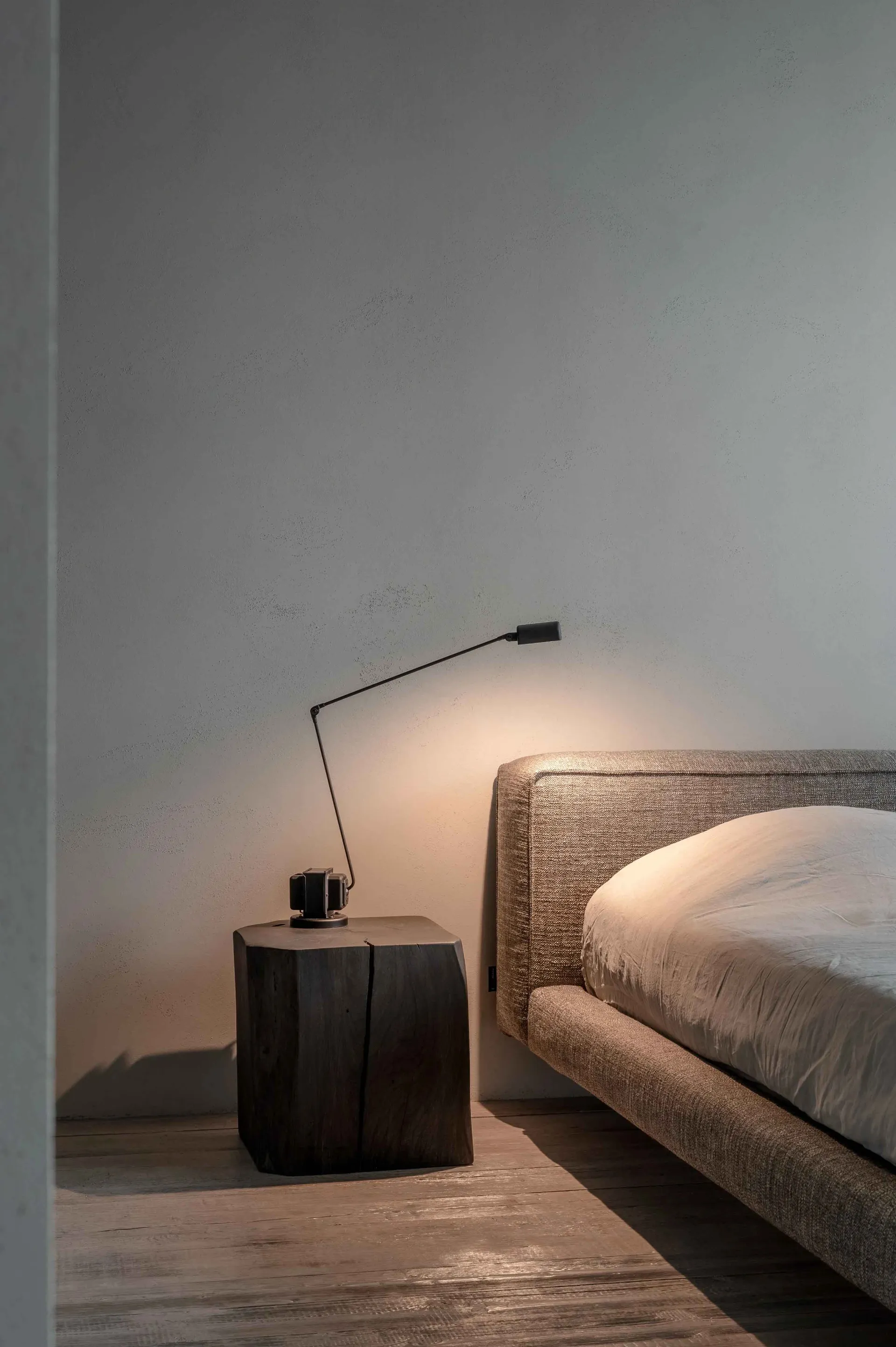 A modern bedroom featuring a textured upholstered headboard and a wooden bedside table with a sleek lamp.