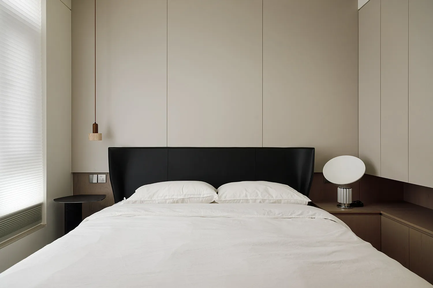 A modern minimalist bedroom featuring a white bed with black headboard, white bedding, and wooden accents.