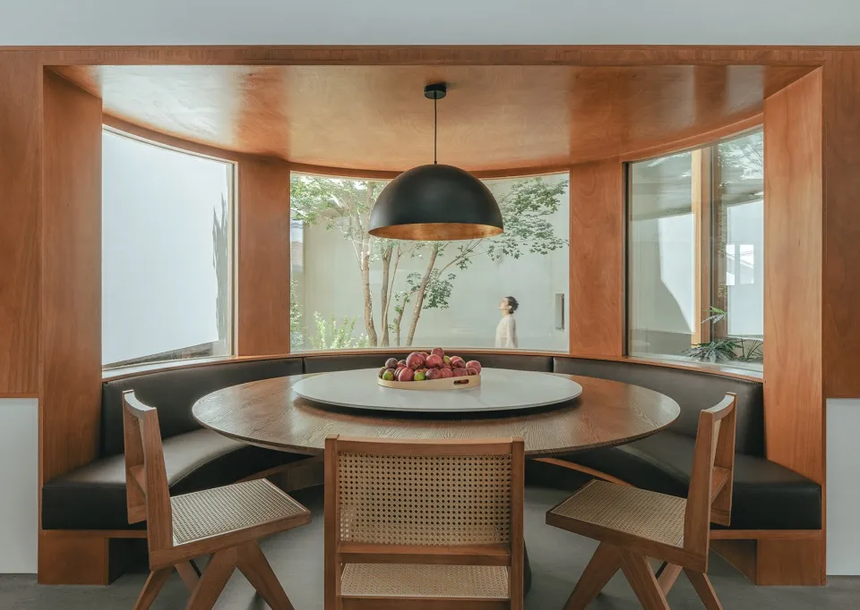 Modern dining area with round table, seating banquette, and black pendant light.