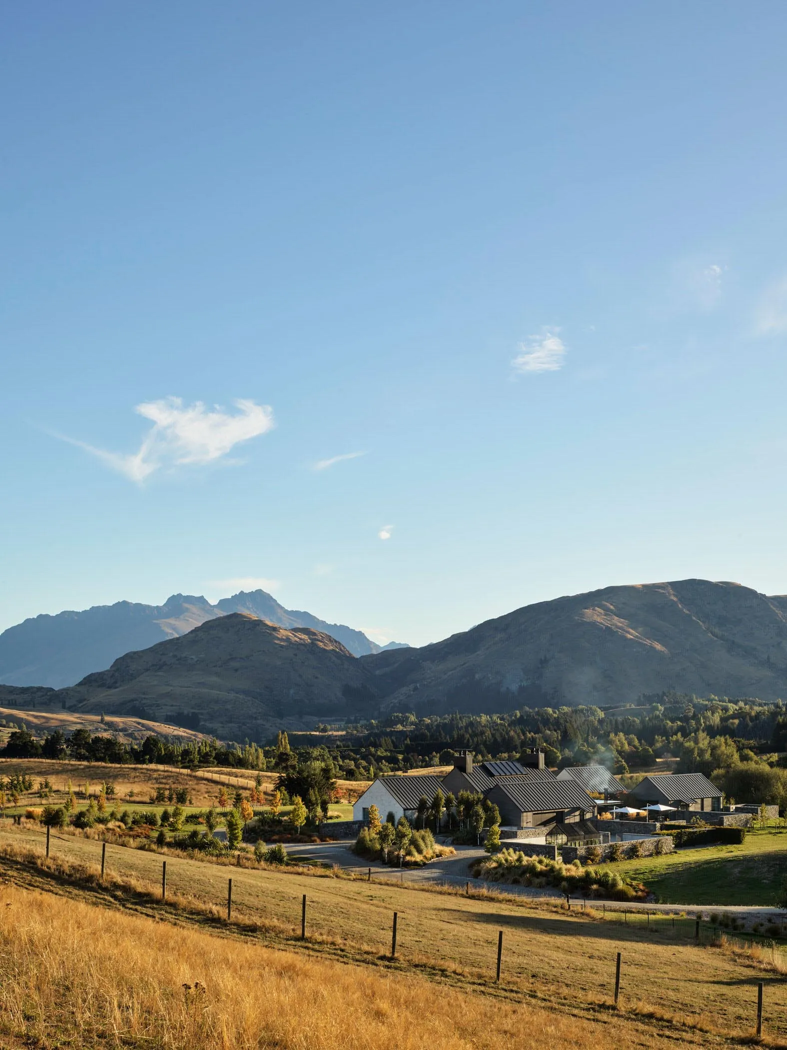 A serene rural landscape featuring a picturesque village nestled amidst mountains, with a clear blue sky above and a tranquil