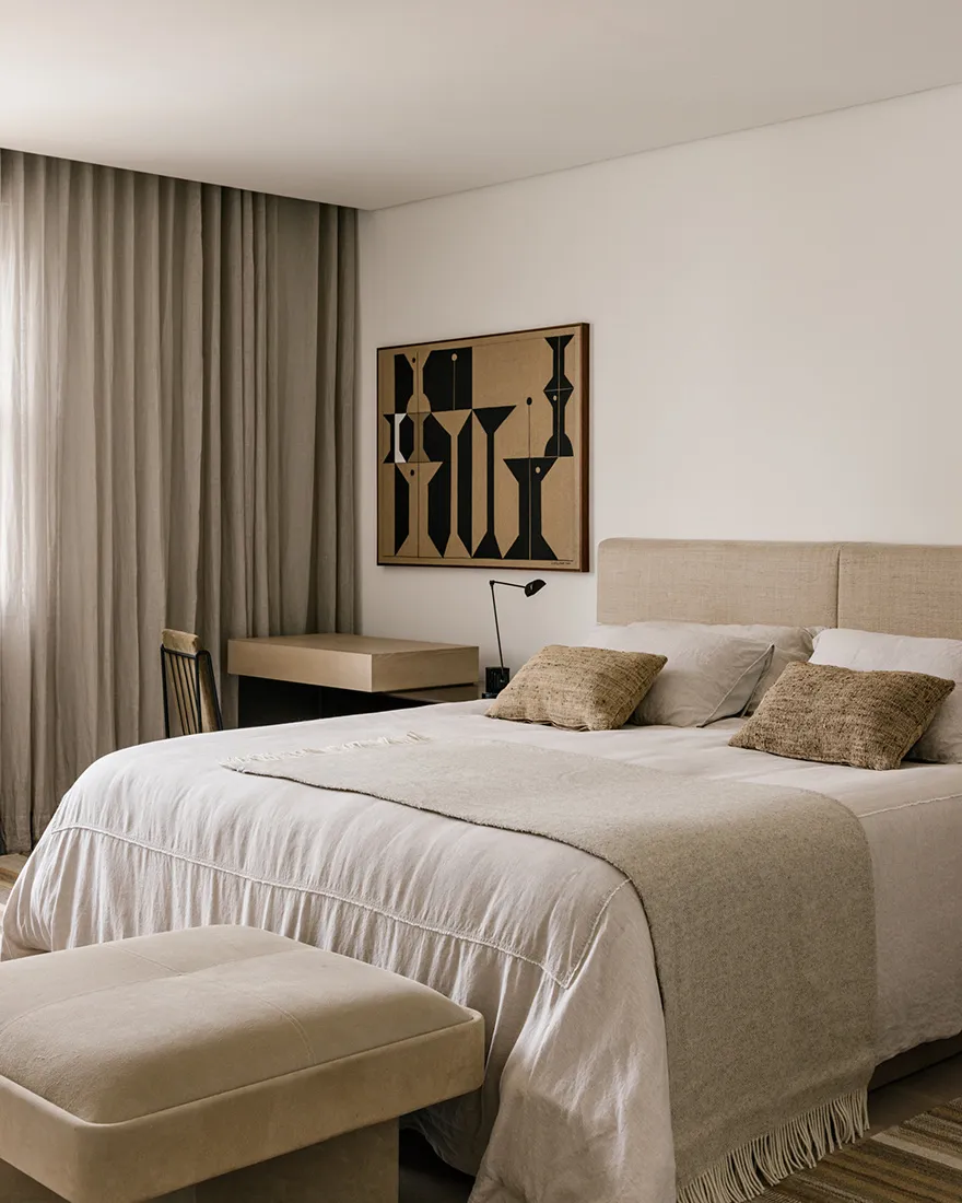 A minimalist bedroom featuring textured fabric bedding and a simple, geometric artwork on the wall.