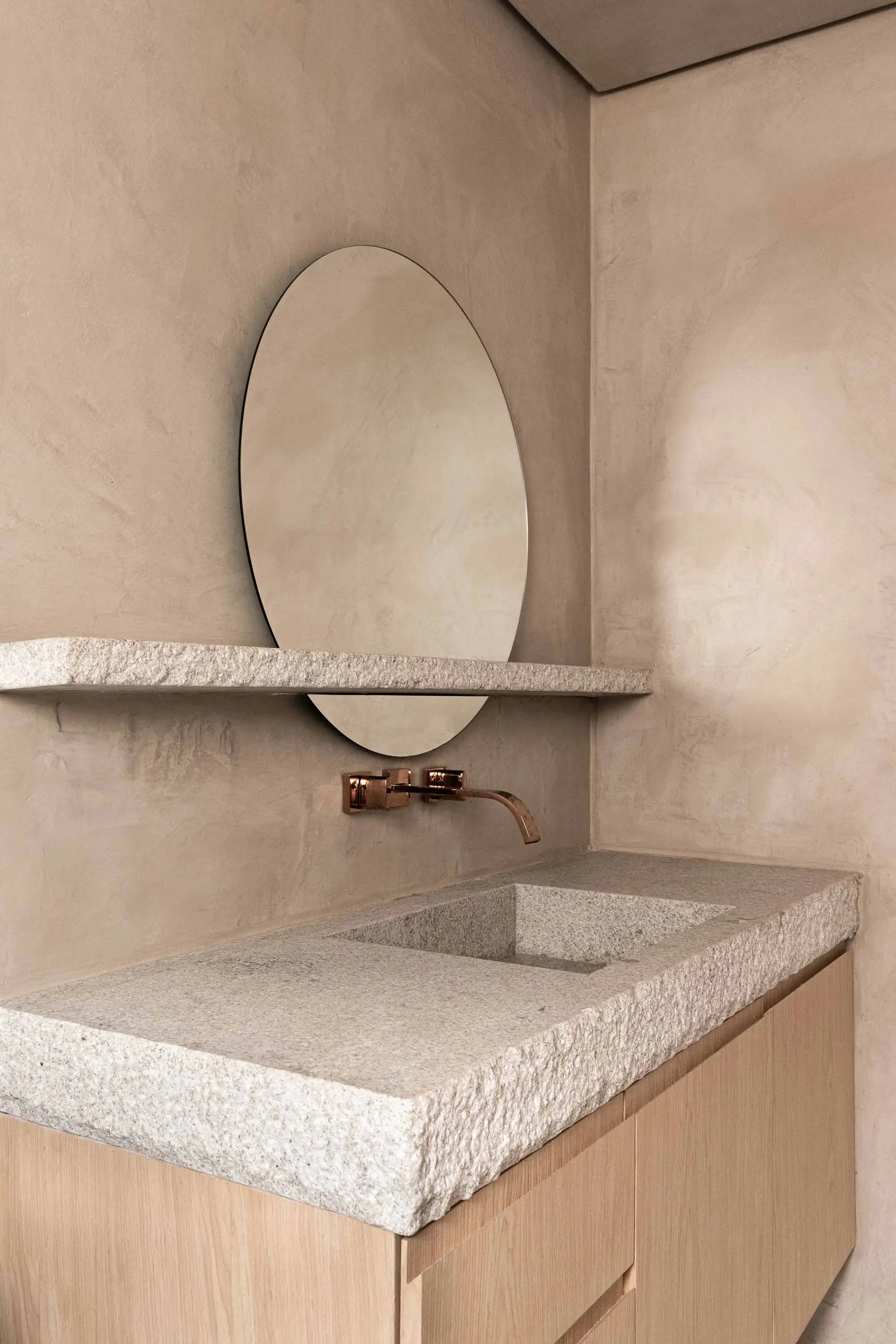 A minimalist bathroom featuring a granite countertop sink and a round mirror on the wall.