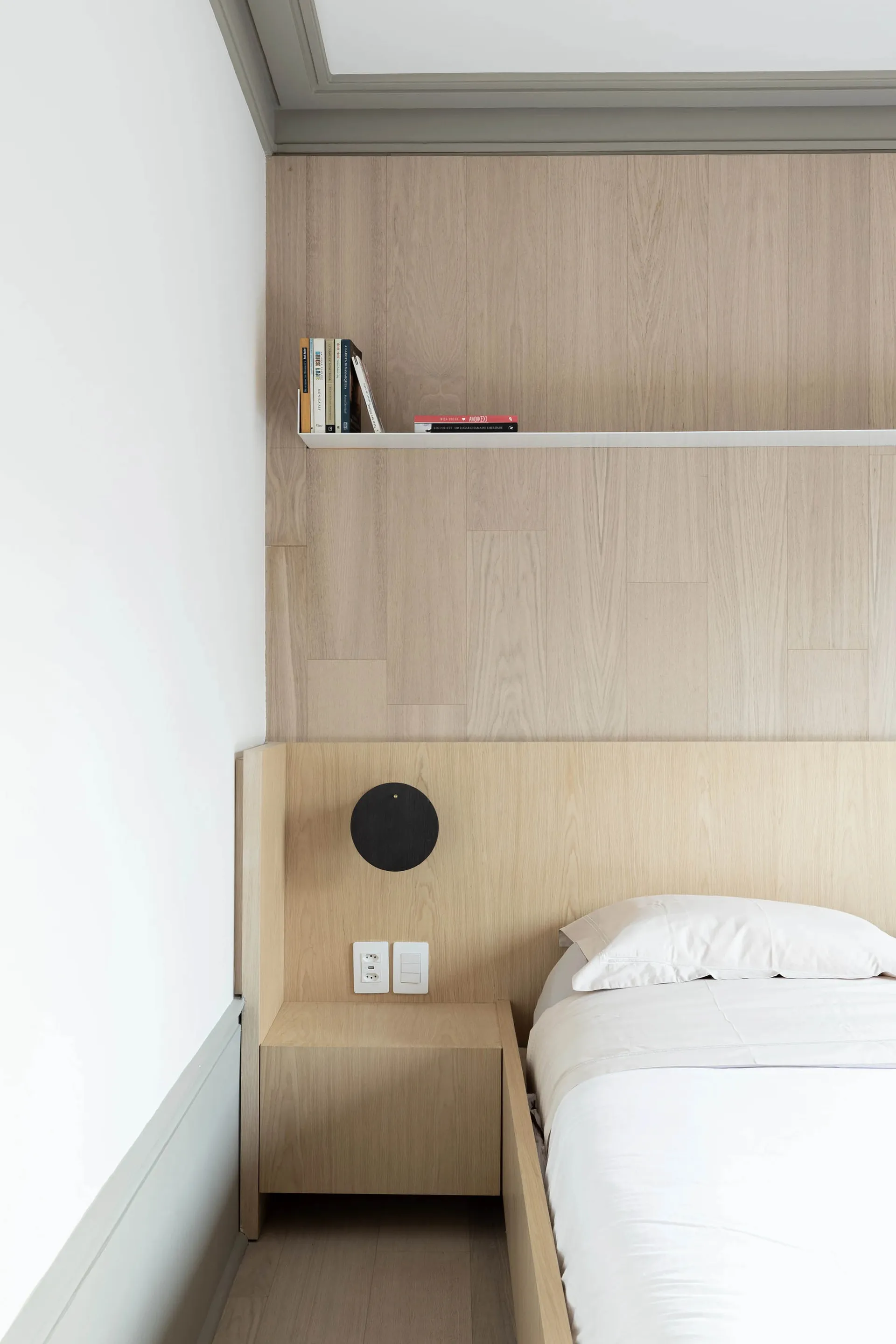 A minimalist bedroom featuring wooden furniture, white bedding, and a mounted clock.