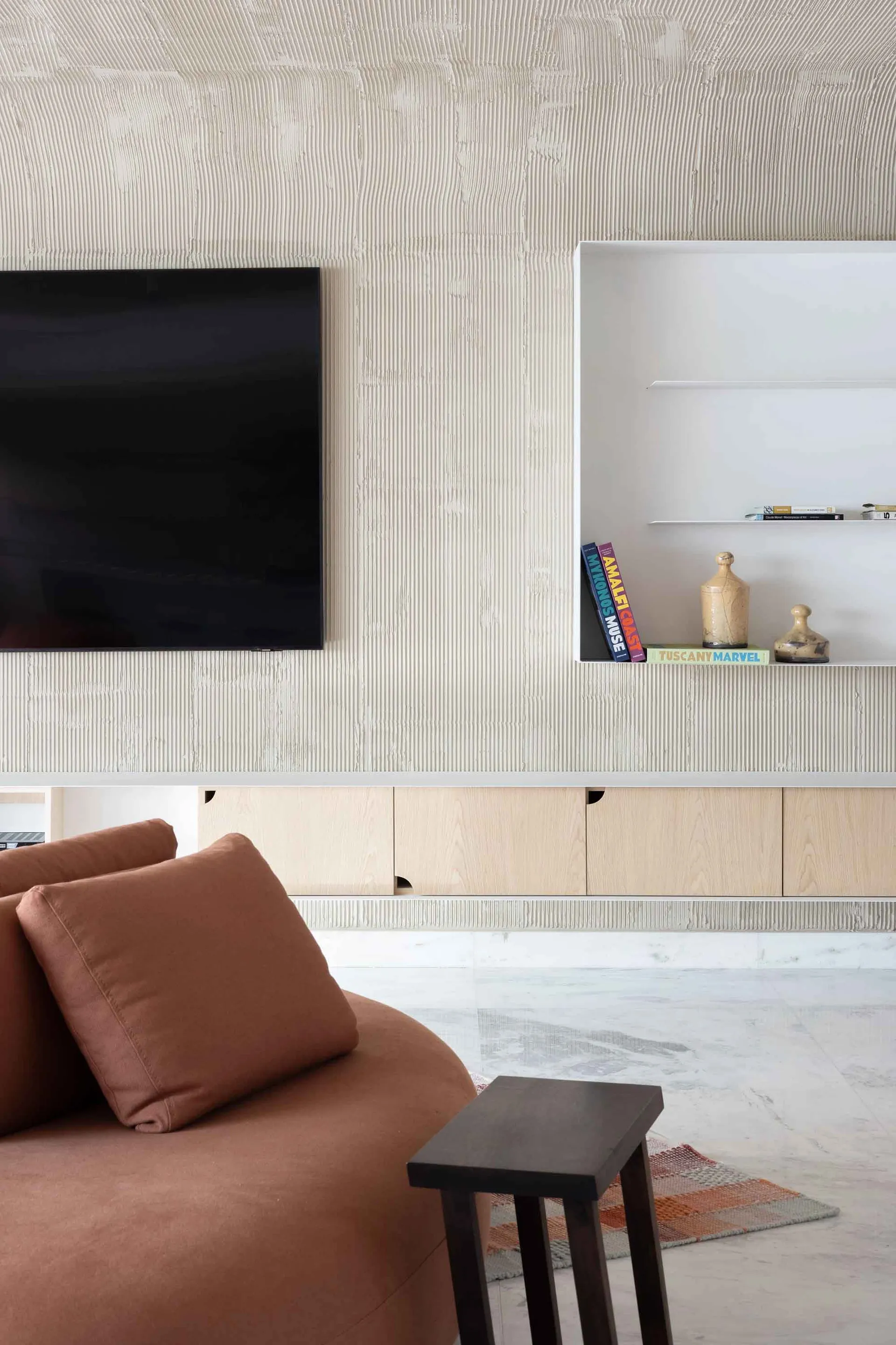 A minimalist living room featuring concrete-textured walls and a television unit with floating shelves and a bookcase below.