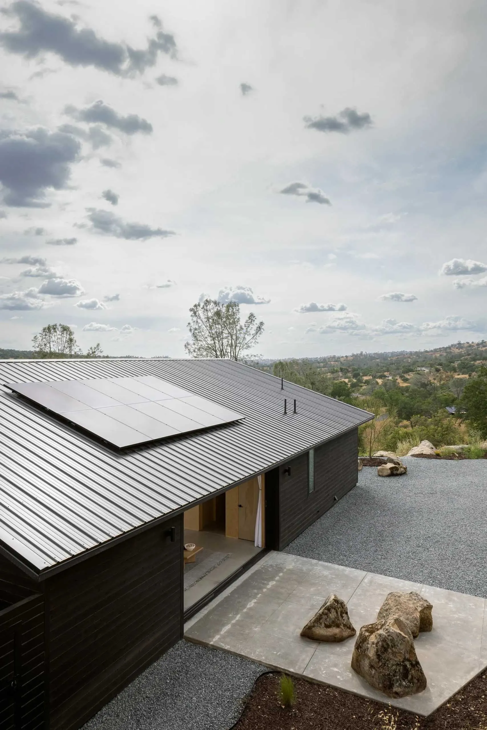 A minimalist residential exterior with a metal roof and stone features.