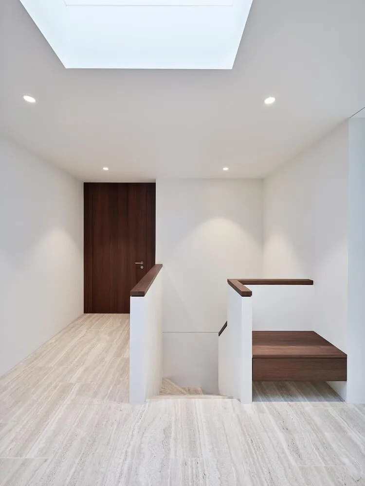 Modern minimalist hallway with white walls, marble flooring, and wooden accents.