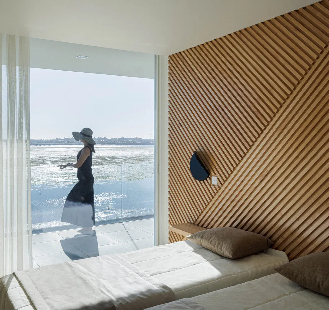 A modern bedroom featuring a bed with a wooden headboard and an ocean view.