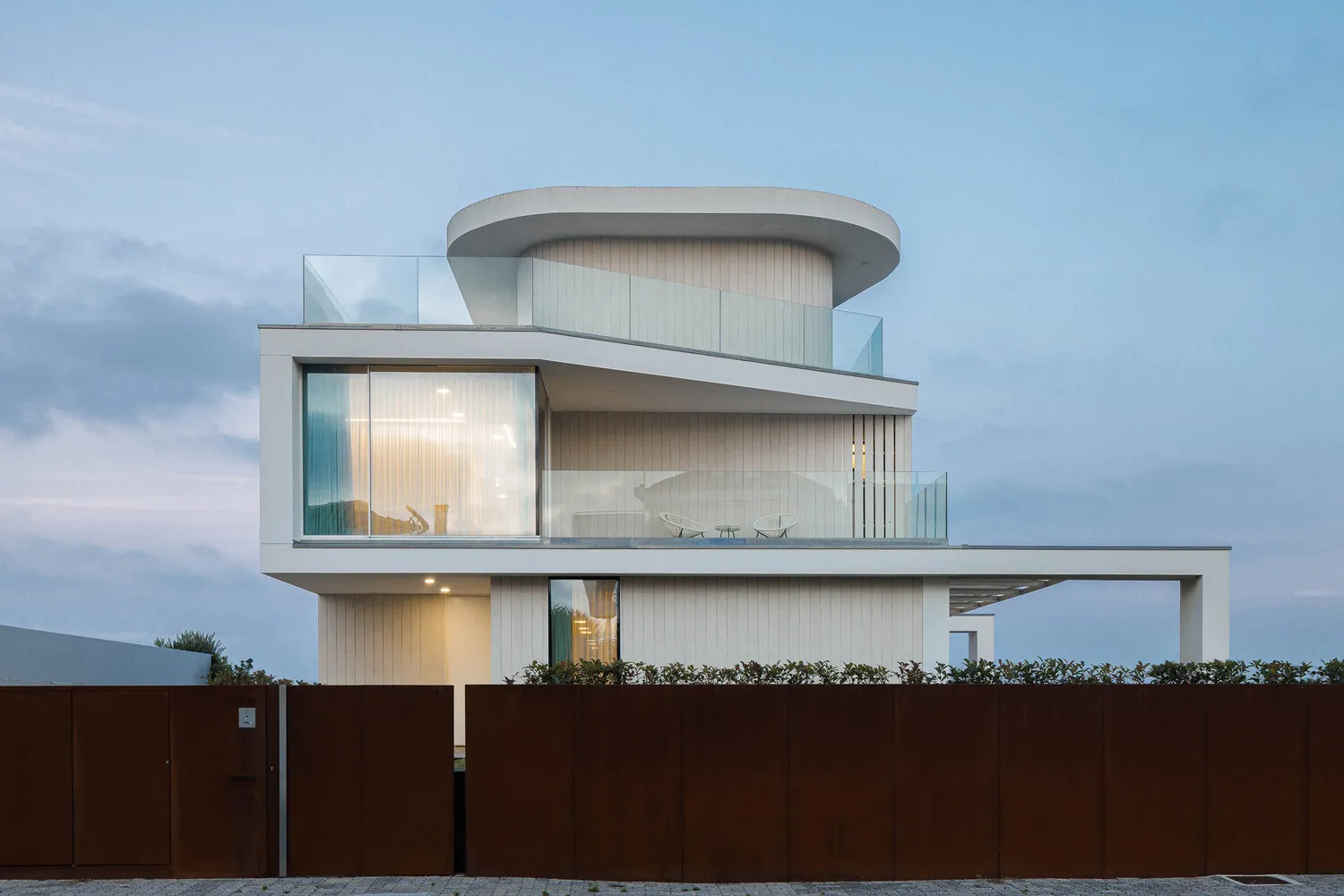 Modern residential house with metal cladding and wood panels, featuring large glass windows and a curved roof.