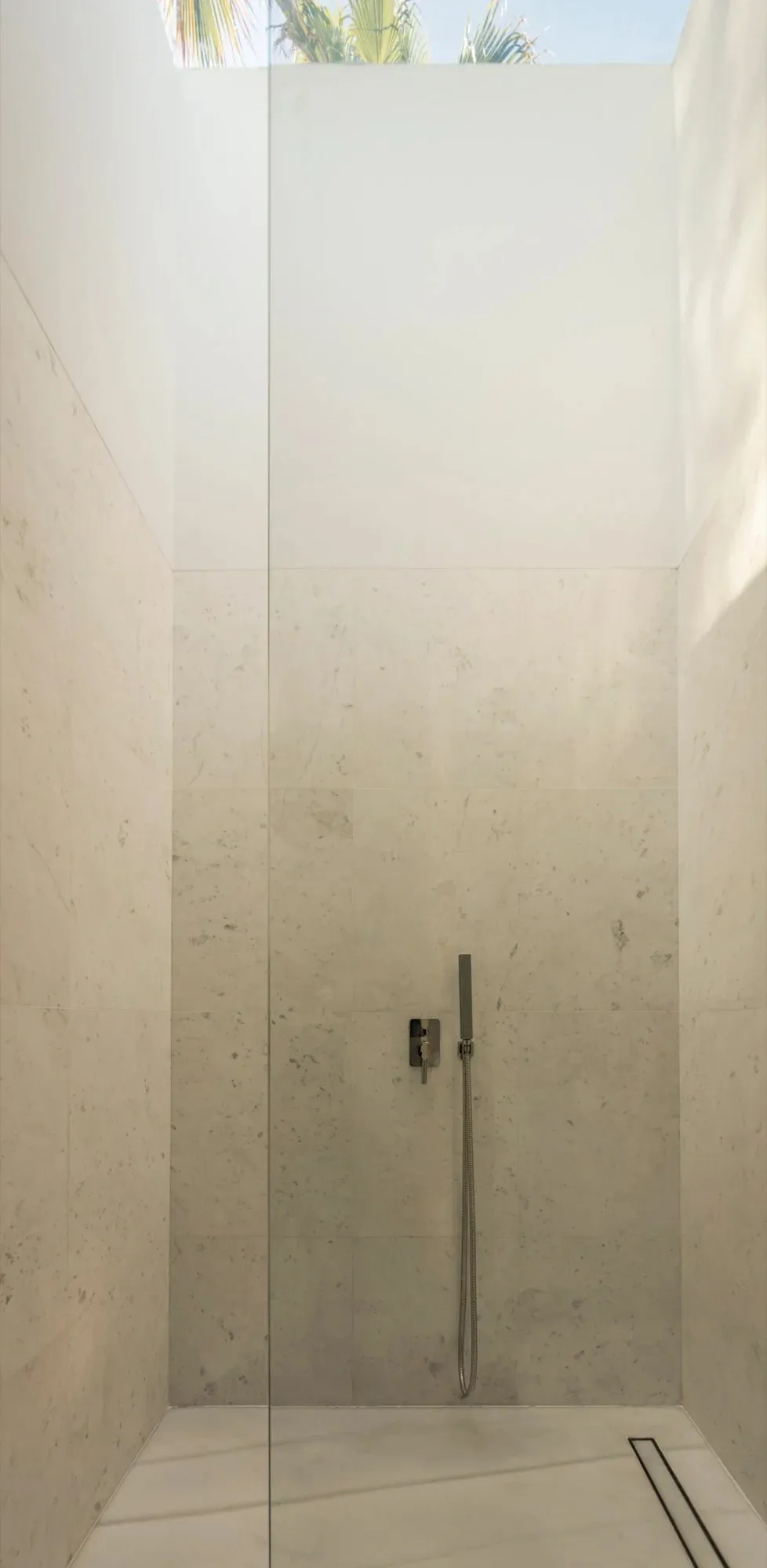 Modern minimalist bathroom with white marble walls and floor, featuring a sleek shower head.