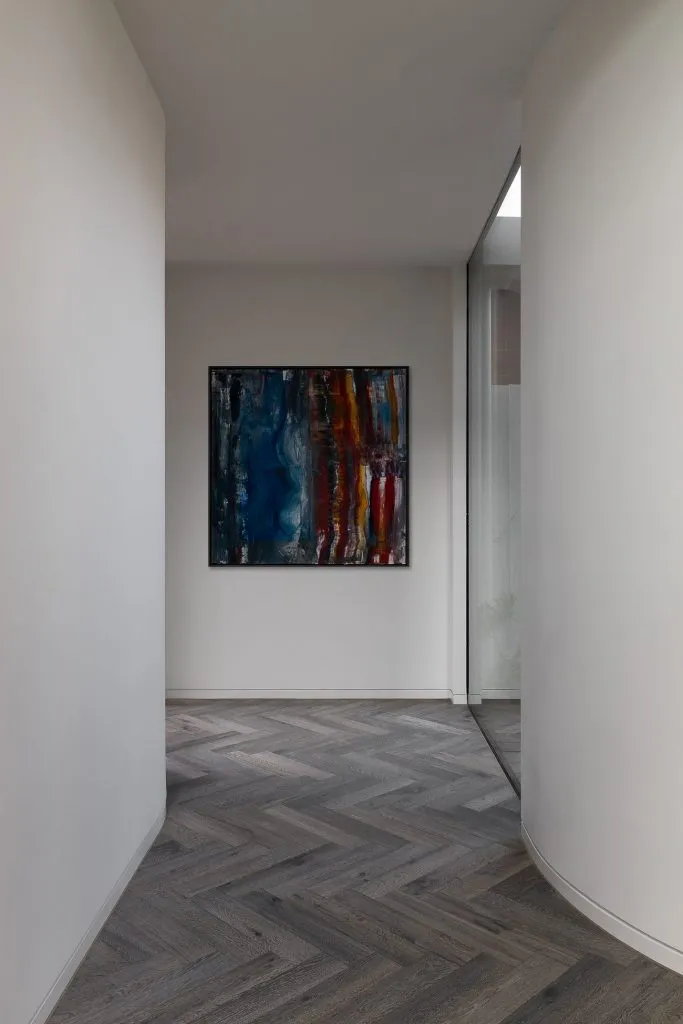 A modern corridor featuring a wooden floor and an abstract painting on the wall.