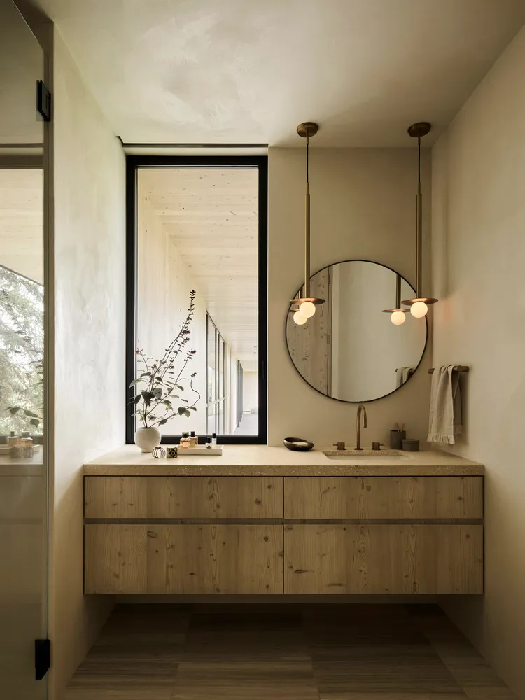 A modern minimalist bathroom with wooden elements and a round mirror above a sink.