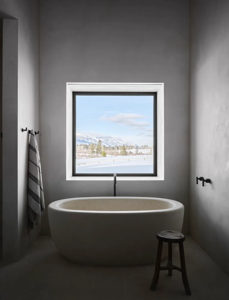 Modern bathroom with a concrete bathtub, designed with a minimalist aesthetic, featuring a window with a scenic view.