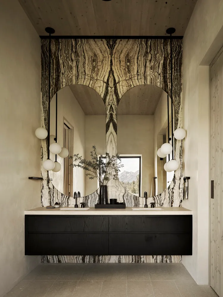 A minimalist bathroom featuring a marble vanity and sink, with a large mirror and spherical lights.
