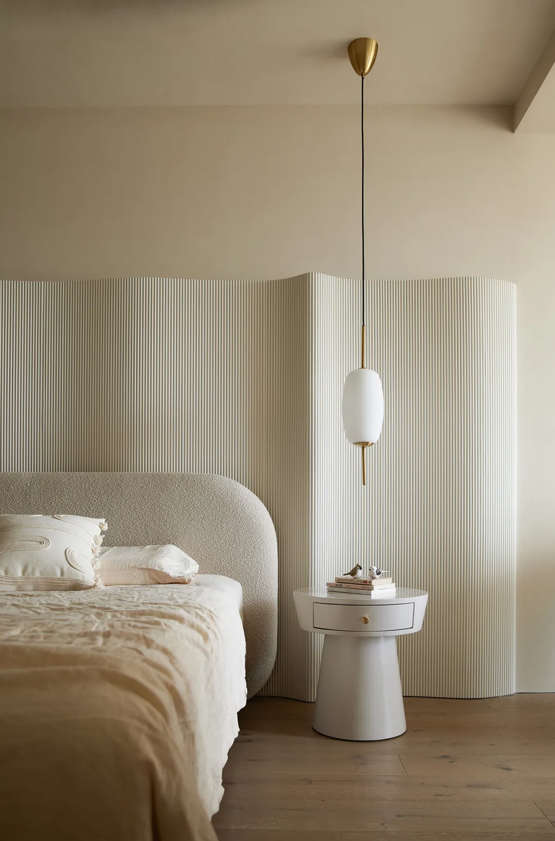 A minimalist bedroom featuring a textured fabric bed against a ribbed wall and a modern pendant light above a sleek, white be