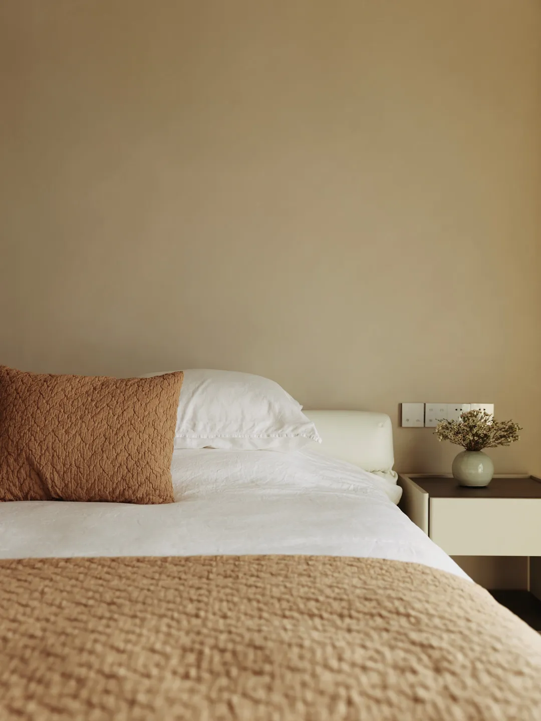 Minimalist bedroom with bed, pillows, blanket, nightstand, and vase with flowers