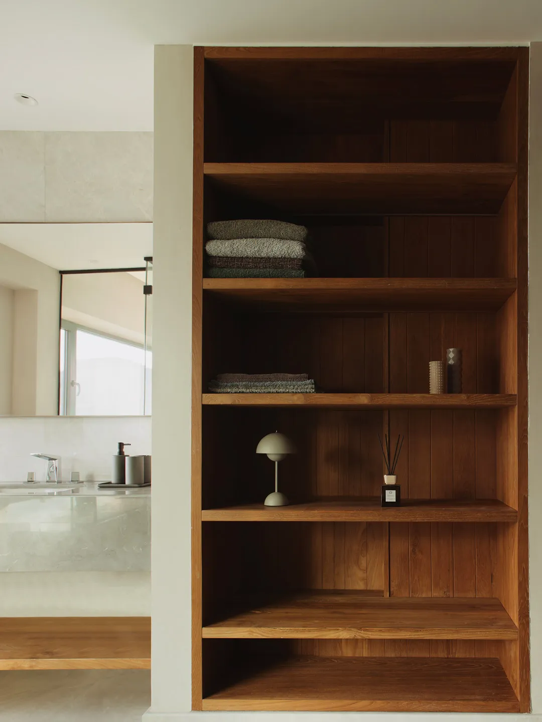 A modern bathroom with wooden shelving holding towels and decorative items.