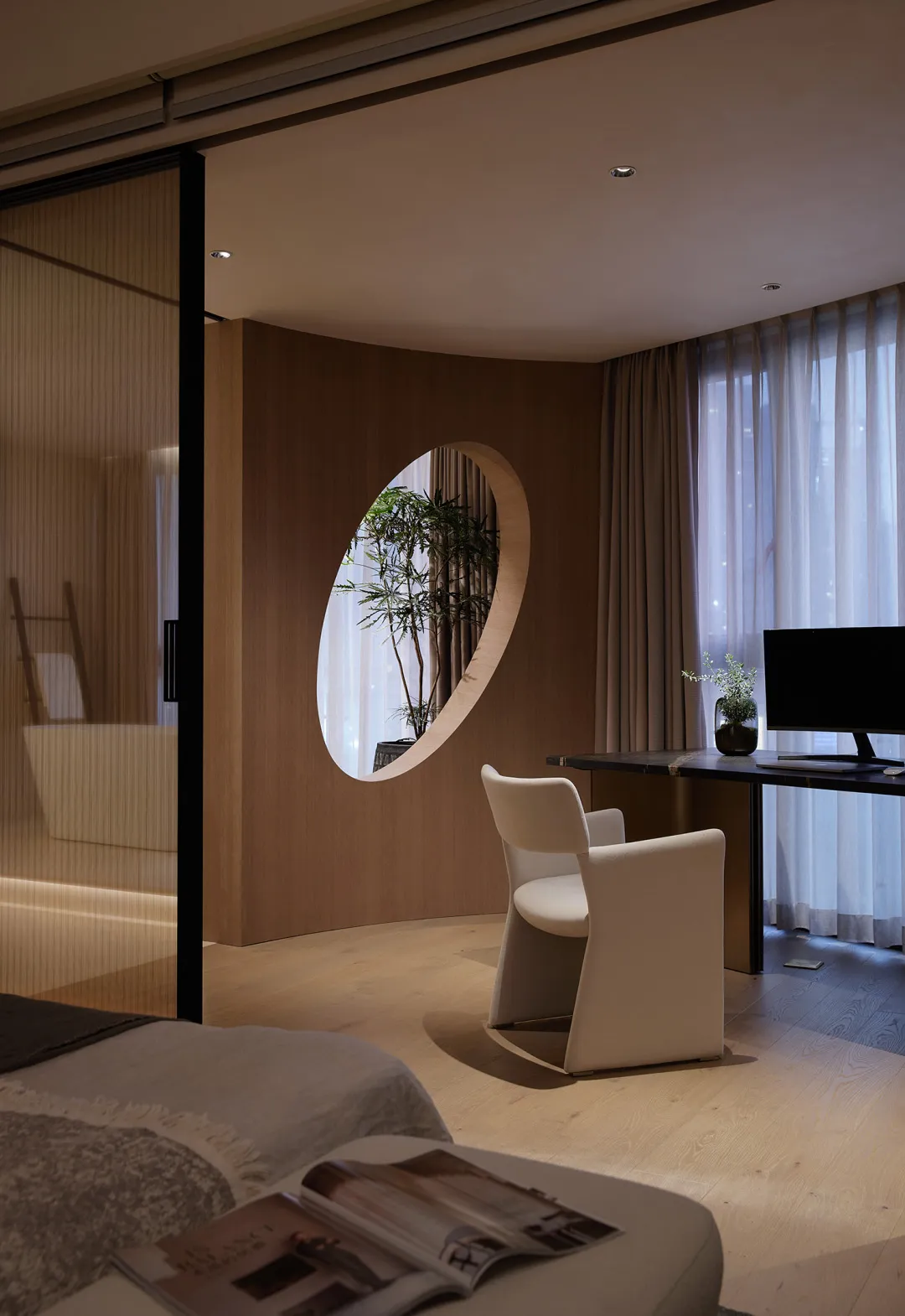 A minimalist office space featuring a transparent oval window overlooking greenery.